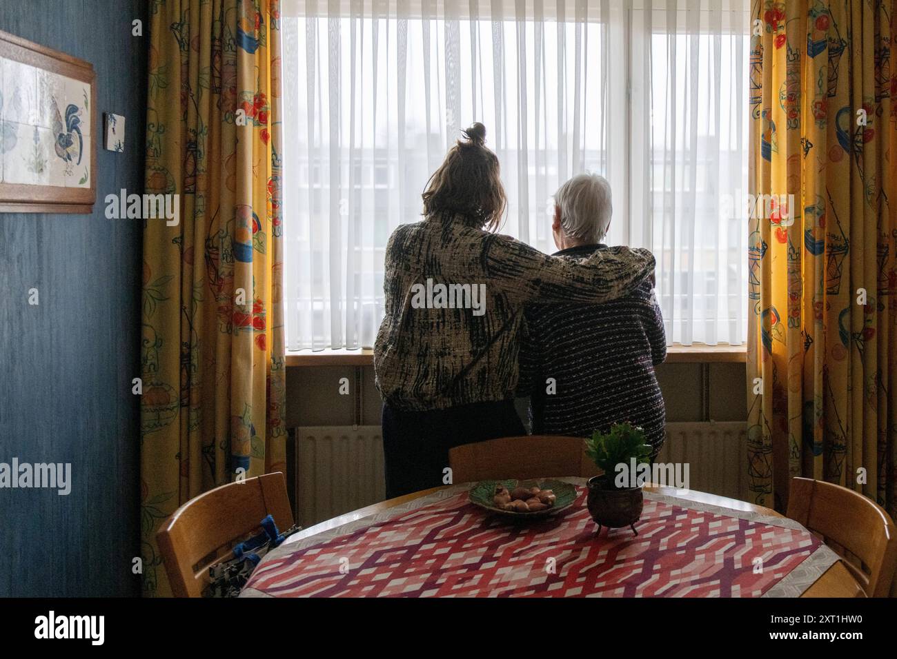 Ouderdom Una giovane donna e una donna anziana stanno insieme vicino a una finestra, guardando fuori da una stanza accogliente. Molenhoek Nederland panc05358 Copyright: XCO Foto Stock