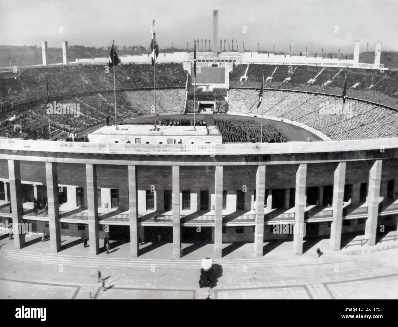 La fotografia mostra l'Olympiastadion di Berlino, il fulcro del Reichssportfeld, costruito dalla Germania nazista per le Olimpiadi del 1936. Lo stadio, con la sua struttura imponente, copriva un'area di 17.152 metri quadrati e poteva ospitare 115.000 spettatori. Era circondato da 136 pilastri di pietra calcarea, con due torri alte 35 metri sul fronte orientale, a simboleggiare la grandezza e l'ambizione del regime nazista durante questo evento globale. Foto Stock