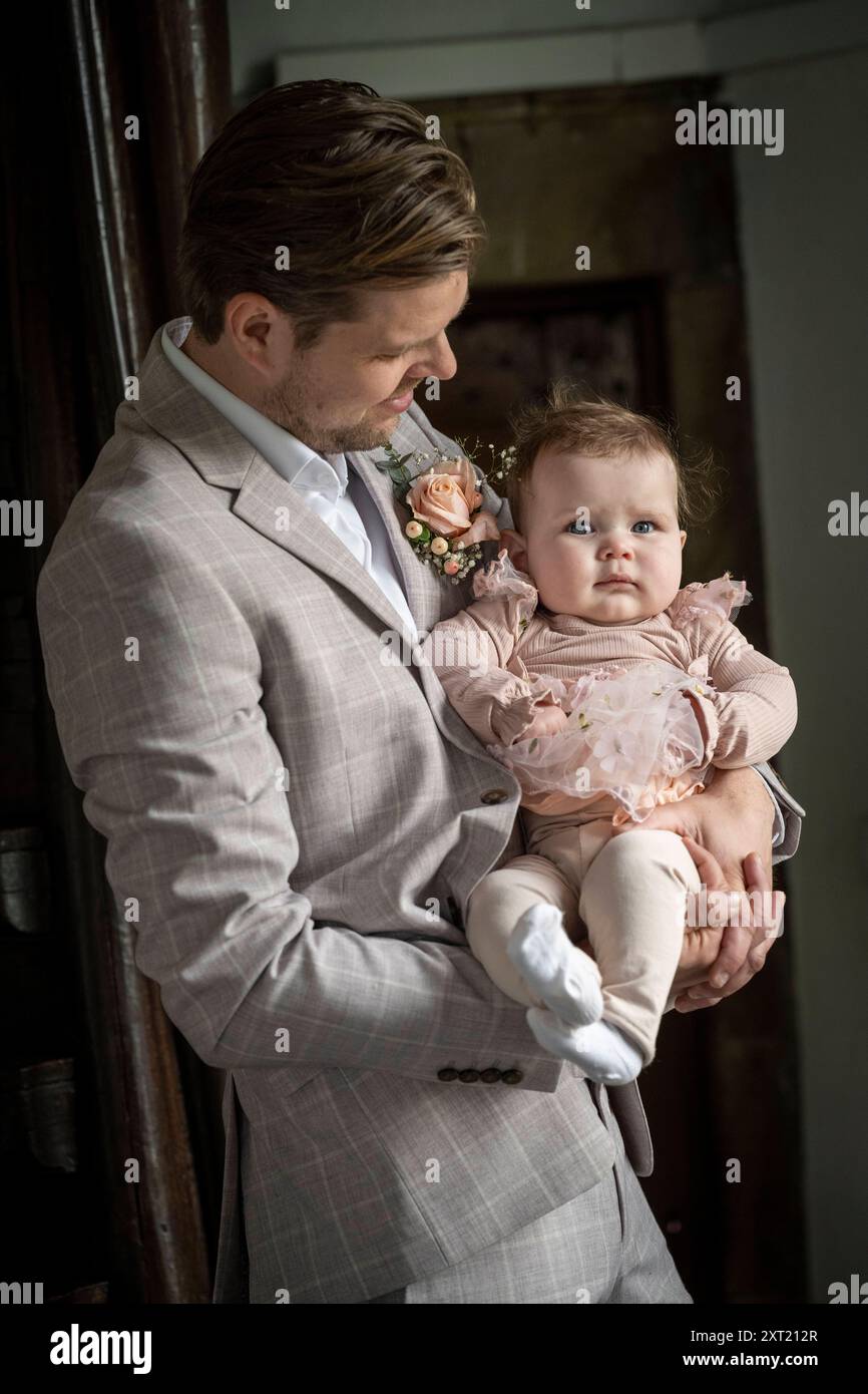 Un uomo ben vestito tiene una bambina con un vestito rosa in occasione di un evento formale. Panc05835 Copyright: XConnectxImagesx Foto Stock