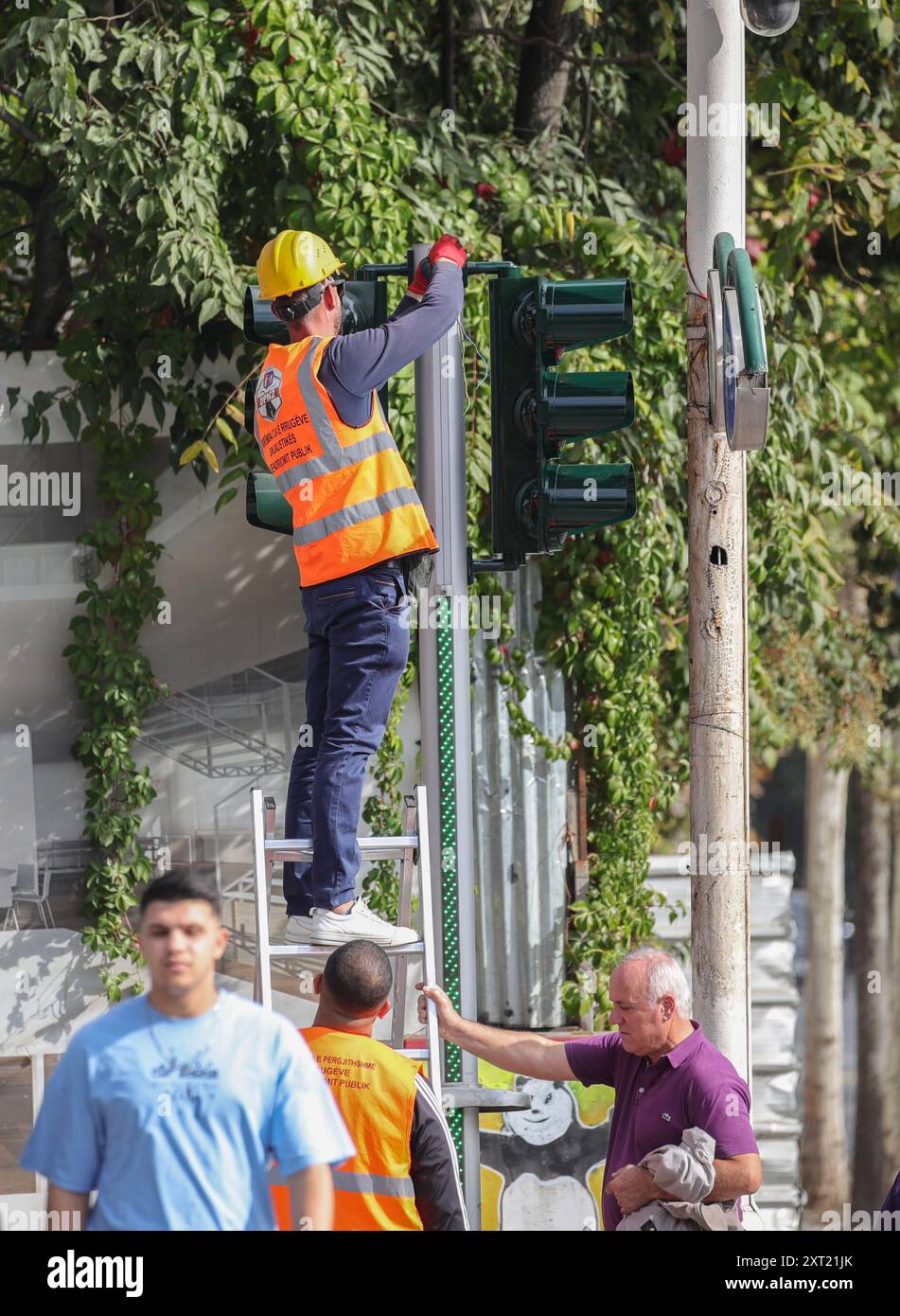 Tirana, Tirana, Albania. 13 agosto 2024. Un uomo albanese aiuta a mantenere la scala di un lavoratore municipale mentre ripara un semaforo a Tirana, Albania. (Credit Image: © Armando Babani/ZUMA Press Wire) SOLO PER USO EDITORIALE! Non per USO commerciale! Foto Stock