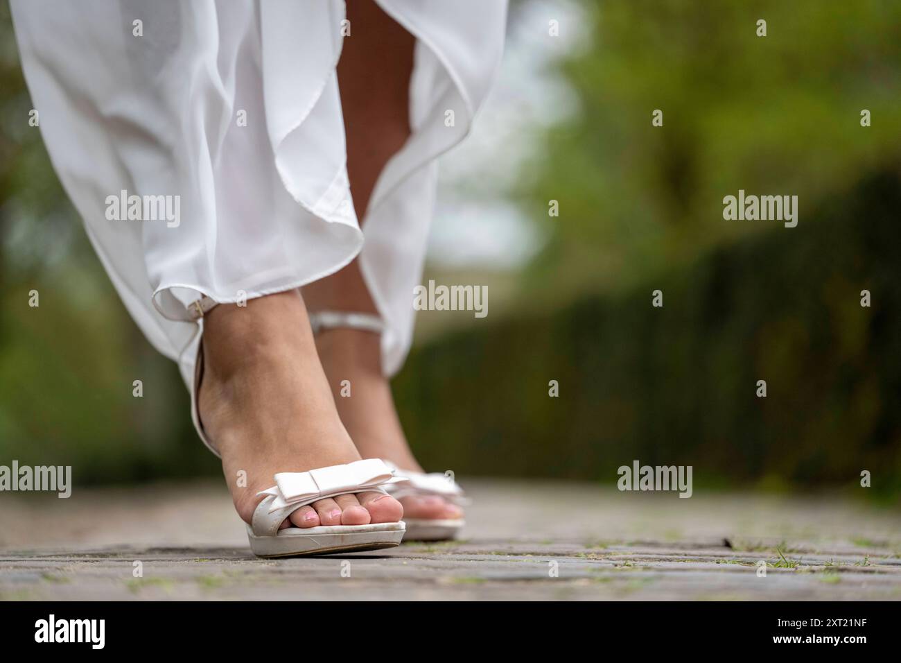 Primo piano della parte inferiore delle gambe di una persona vestita con un indumento bianco, che cammina su un sentiero lastricato con sandali bianchi. Panc05913 Copyright: XConnectxImagesx Foto Stock