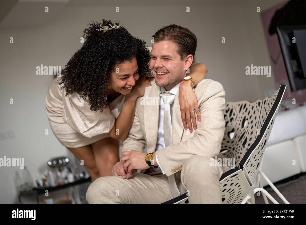 Coppia felice che ride e si abbraccia mentre si siede su una sedia in una stanza ben illuminata. Panc05945 Copyright: XConnectxImagesx Foto Stock