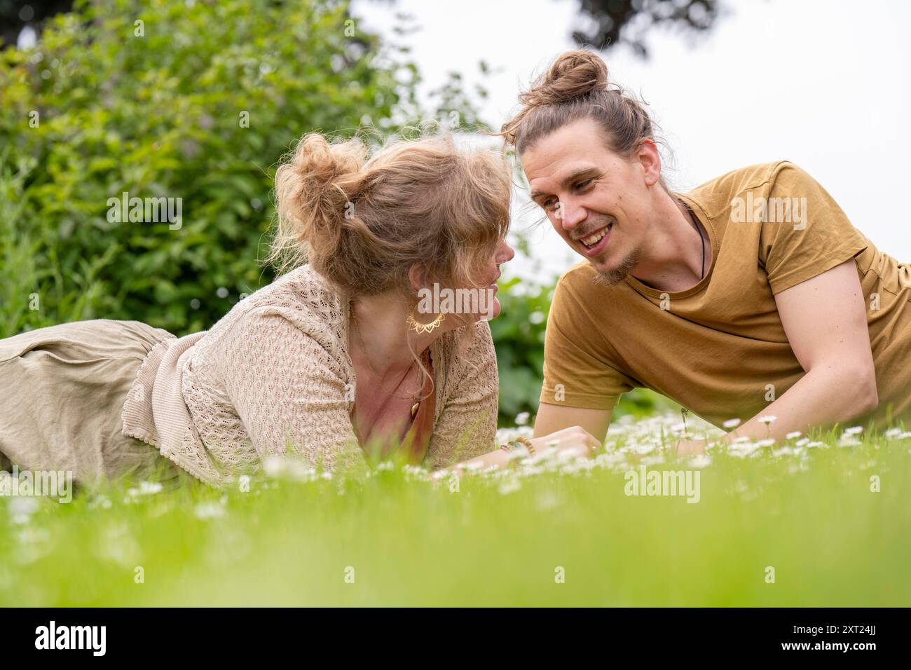 Un uomo e una donna sorridenti sdraiati sull'erba, guardarsi e godersi una piacevole conversazione all'aperto. Panc06184 Copyright: XConnectxImagesx Foto Stock