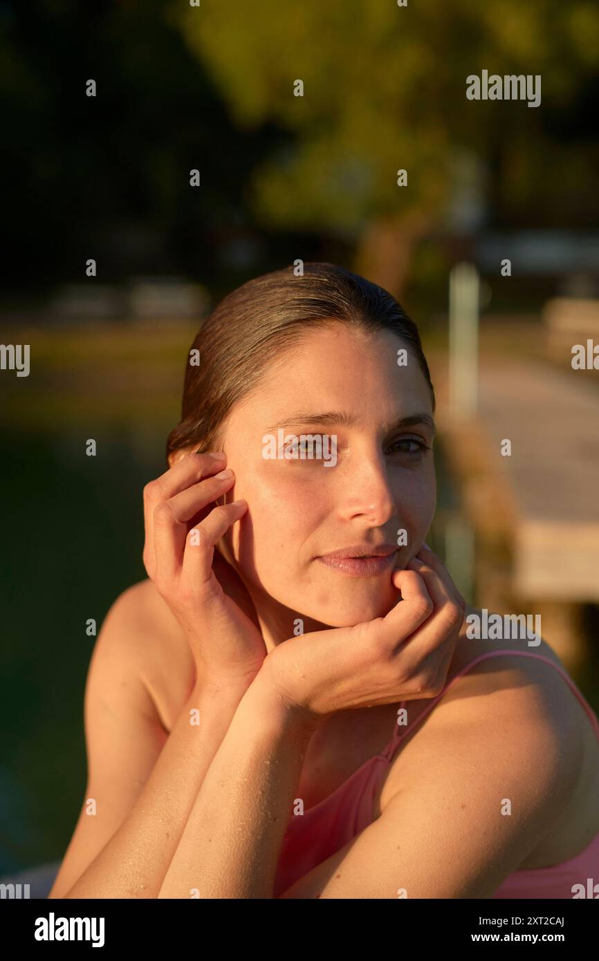 Donna sorridente che posa al tramonto sull'acqua con la mano sulla guancia, trasudando un senso di calma. Bola03033 Copyright: XConnectxImagesx Foto Stock