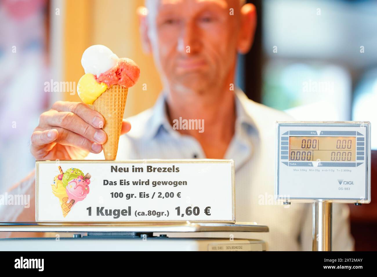 PRODUZIONE - 13 agosto 2024, Baden-Württemberg, Gaggenau: L'operatore Michael Böhmer mette un gelato in un cono sulla bilancia al Café Brezels. Al Café Brezels, nel centro di Gaggenau, il gelato non viene più caricato dalla paletta ma dal grammo. I clienti pagano due euro per 100 grammi di gelato e il prezzo viene adeguato di conseguenza per quantità minori. Foto: Uwe Anspach/dpa Foto Stock