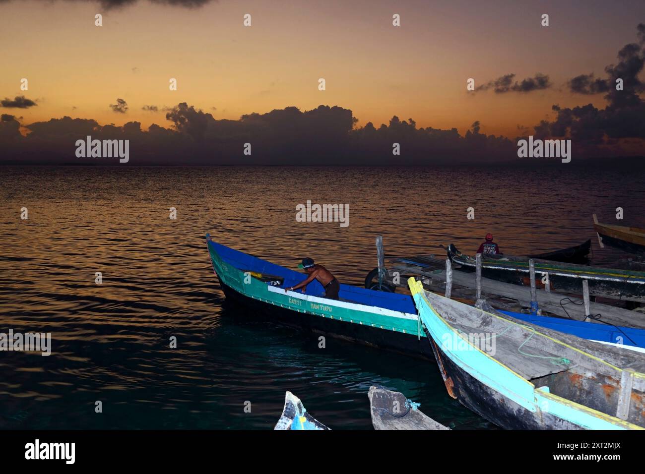Uomo kuna indigeno che svuota una barca da pesca in legno sull'isola di Carti Yandup al tramonto, isole San Blas, Kuna Yala / Guna Yala, Panama Foto Stock