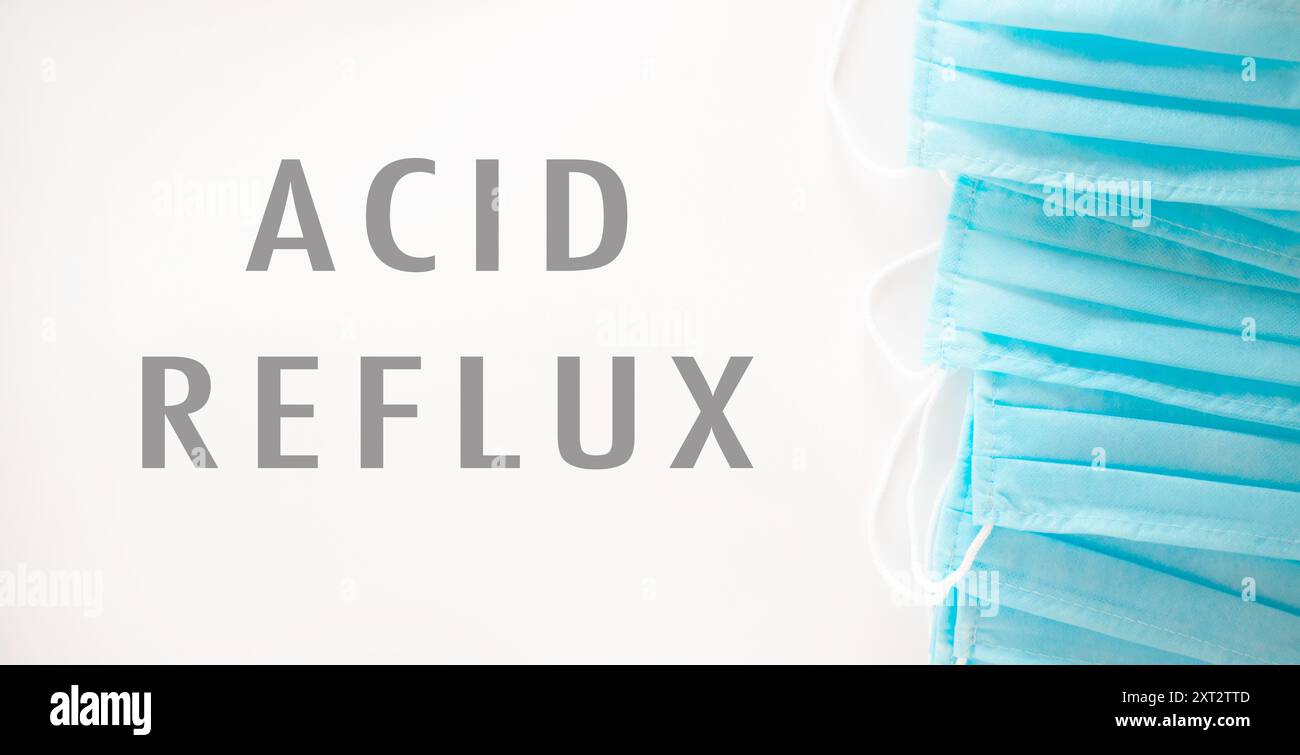Una pila di maschere chirurgiche blu con le parole reflusso acido scritto sotto. Concetto di cautela e importanza di proteggersi dai potenti Foto Stock
