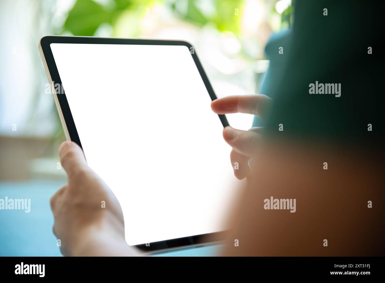 Persona che tiene un tablet con uno schermo vuoto, in un ambiente luminoso e verde. Immagine perfetta per la presentazione di app per tablet, interfacce utente o des grafici Foto Stock