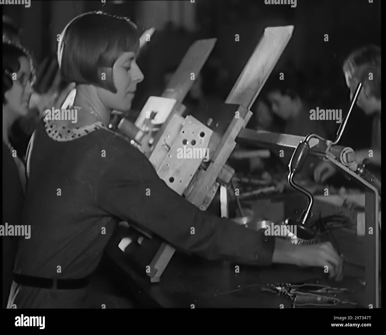 Donne civili che lavorano su una linea di produzione di fabbrica, 1931. "Sally Smith [cioè la donna britannica media] era più probabile che non fosse una lavoratrice ora, impiegando le sue dita agili lungo quelle... linee di produzione di massa. E non importa quanto fosse normale il lavoro, raramente sembrava annoiarsi con esso. Da Time to Remember - A New era, 1931 (Reel 2); documentario sul mondo nei primi anni '1930 Foto Stock