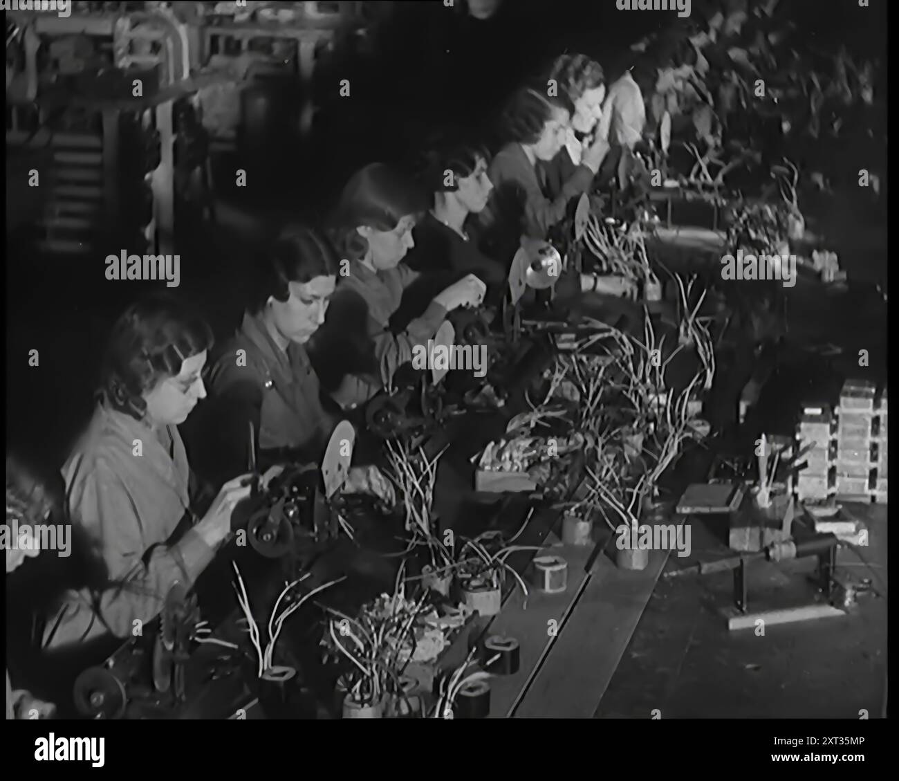 Donne civili che lavorano su una linea di produzione di fabbrica, 1931. "Sally Smith [cioè la donna britannica media] era più probabile che non fosse una lavoratrice ora, impiegando le sue dita agili lungo quelle... linee di produzione di massa. E non importa quanto fosse normale il lavoro, raramente sembrava annoiarsi con esso. Da Time to Remember - A New era, 1931 (Reel 2); documentario sul mondo nei primi anni '1930 Foto Stock
