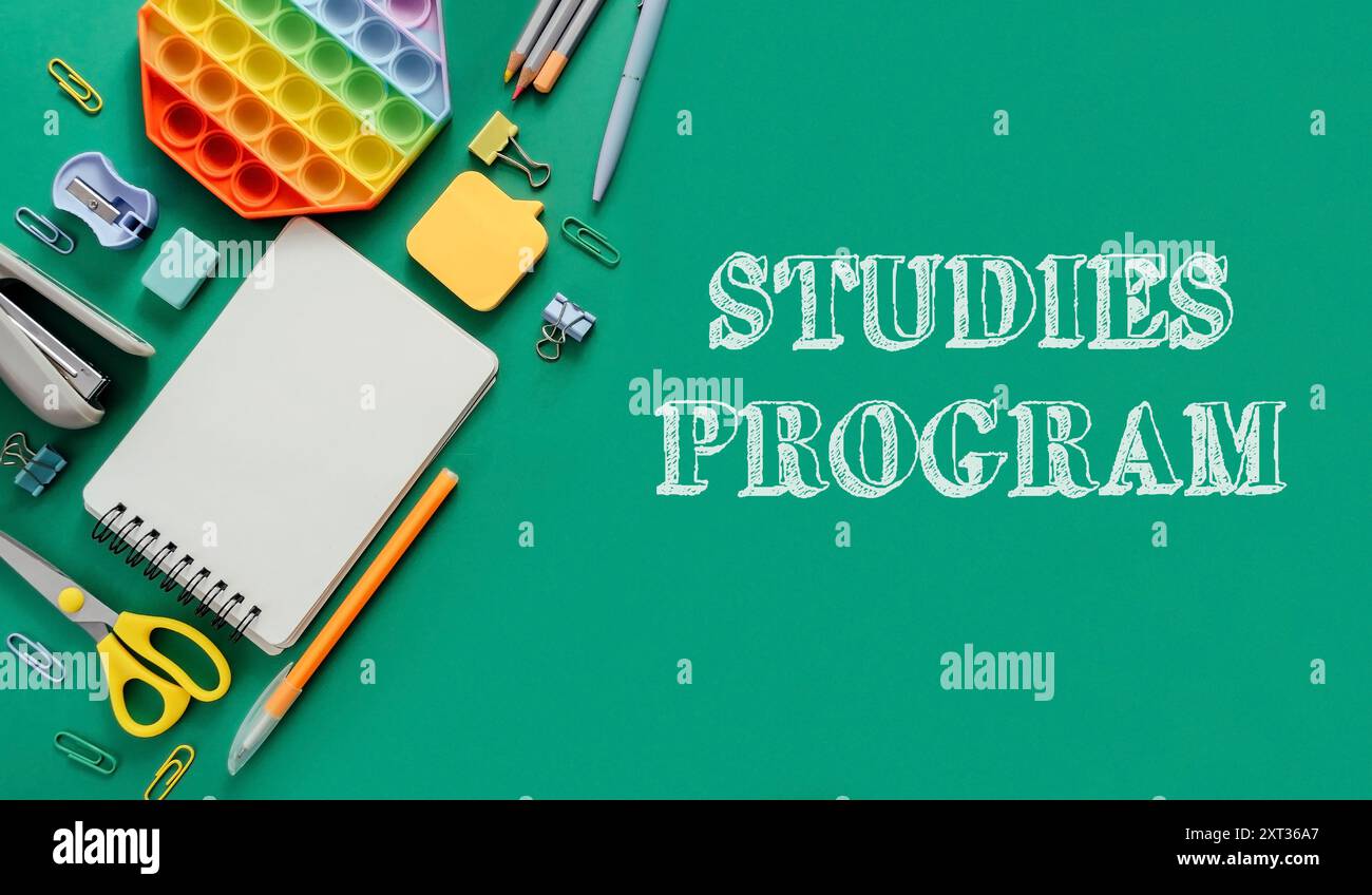Uno sfondo verde con un quaderno, penne e forbici. La parola studi è scritta in lettere bianche sul lato destro dell'immagine Foto Stock