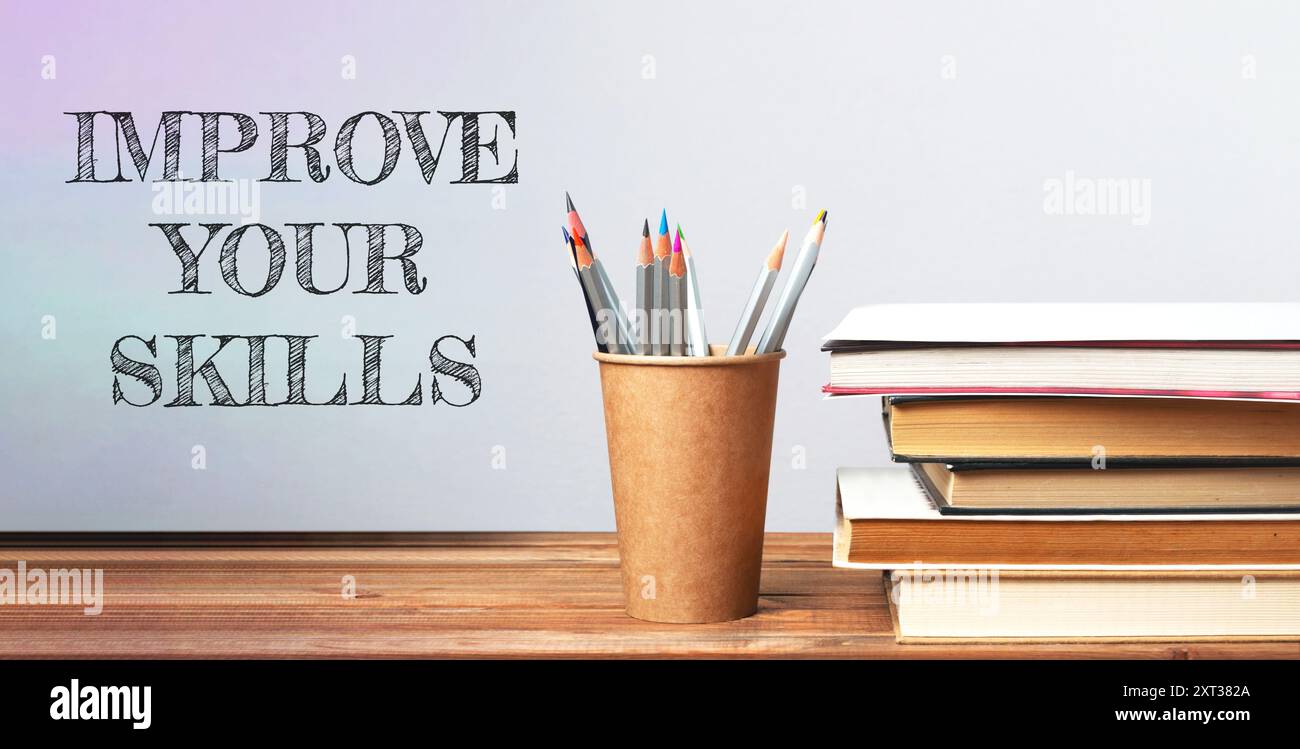 Una scrivania di legno con una tazza di matite e una pila di libri. Le parole che migliorano le tue abilità sono scritte sul muro dietro la scrivania Foto Stock