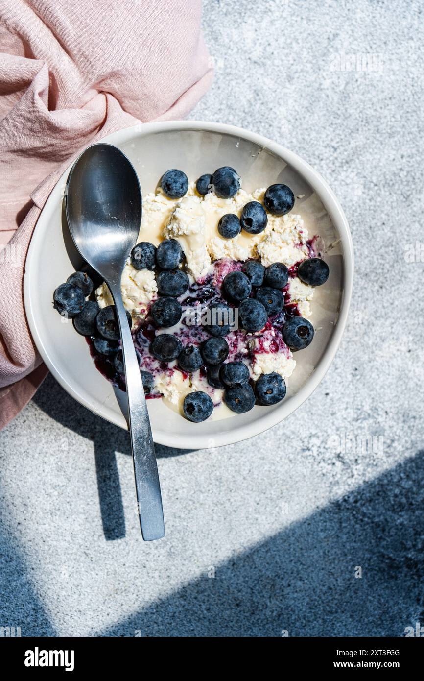 Una nutriente colazione con una ciotola di formaggio fresco condita con marmellata di mirtilli biologici e mirtilli freschi, servita con un cucchiaio d'argento Foto Stock
