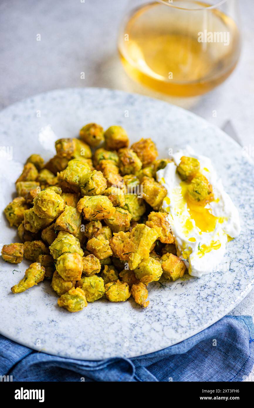 Bamia croccante fritta alla perfezione, servita insieme a una salsa cremosa aromatizzata con aneto e aglio, raffigurata in un ambiente rustico con lo sfondo di un rif Foto Stock