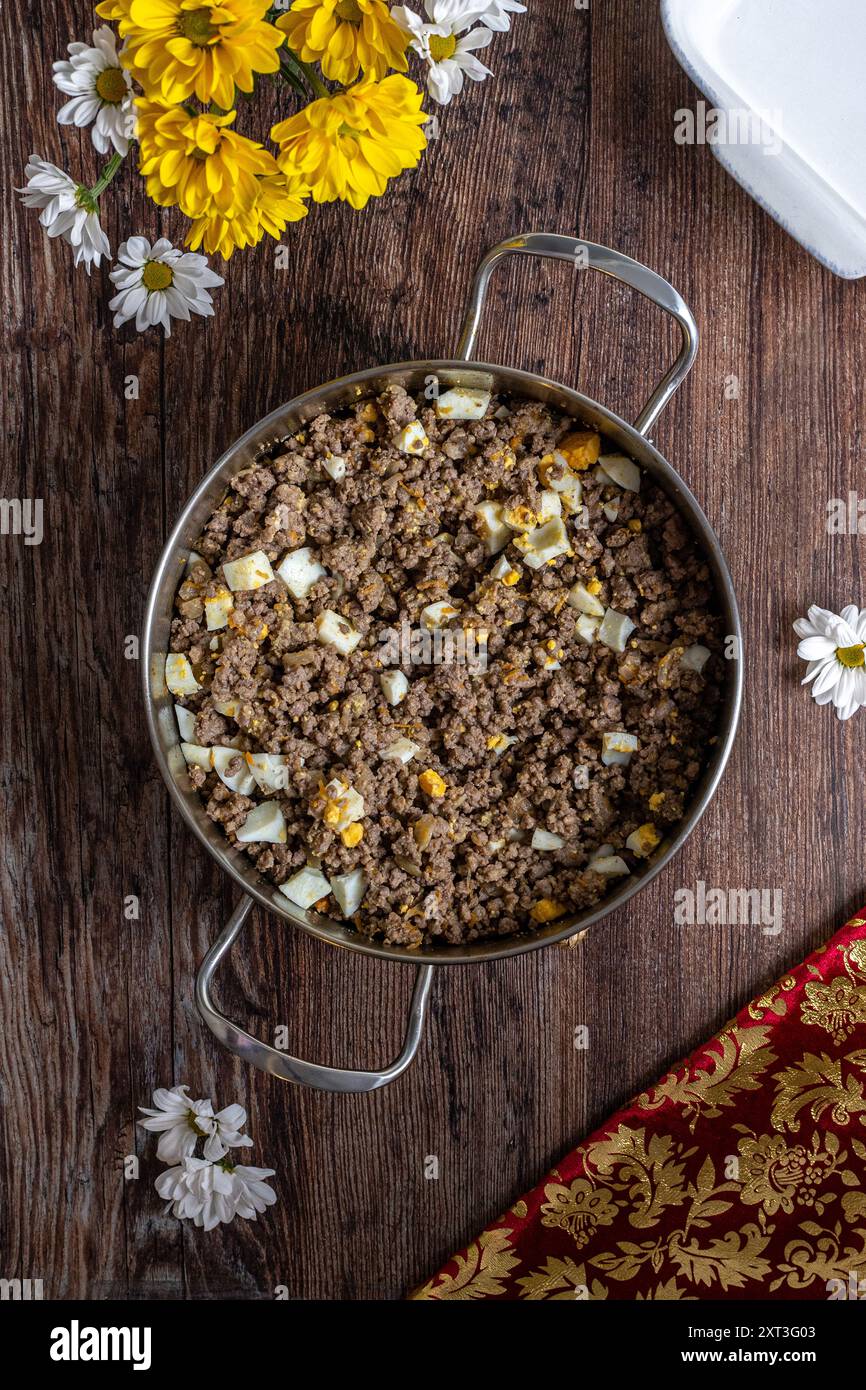 Vista dall'alto di una torta di carne appena preparata fatta in casa ripiena in una padella di acciaio inossidabile, con carne macinata, patate e uova sode su un rustico legno Foto Stock