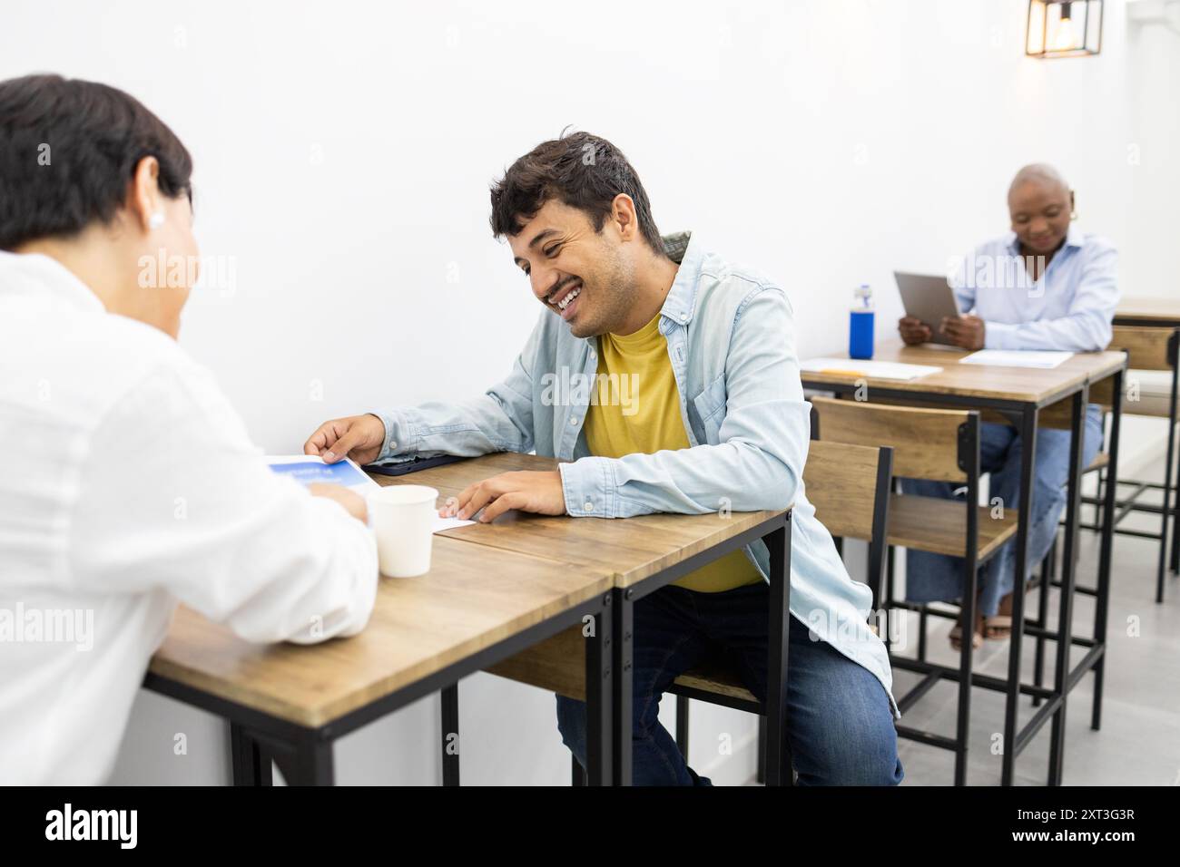 Una scena allegra di studenti adulti che interagiscono in un'accademia di inglese, condividendo pensieri e imparando in modo collaborativo in un ambiente luminoso in classe Foto Stock
