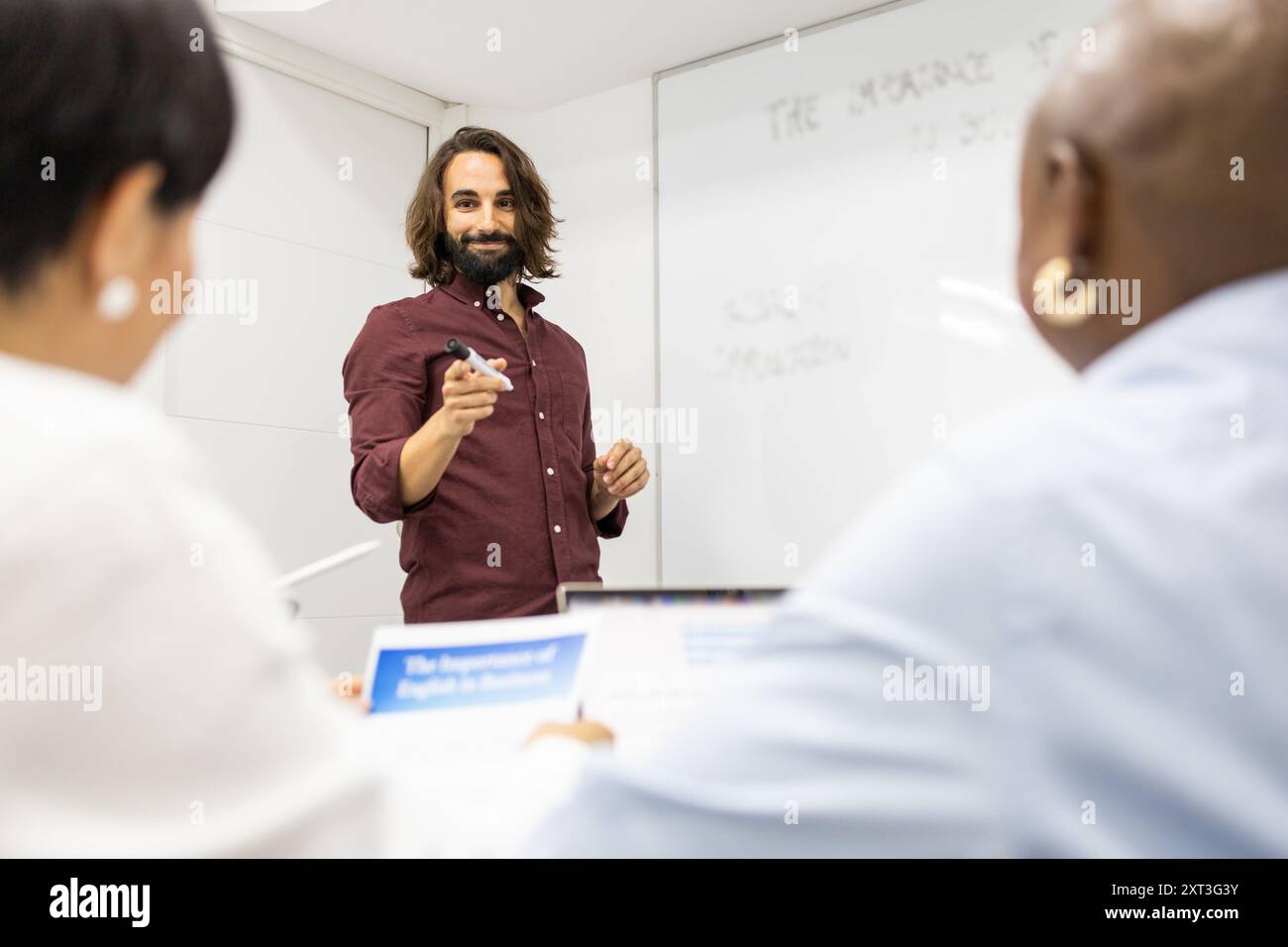 Un'immagine dinamica che cattura un momento educativo coinvolgente all'interno di un'accademia di inglese in cui un gruppo eterogeneo di studenti adulti si concentra su un ma Foto Stock