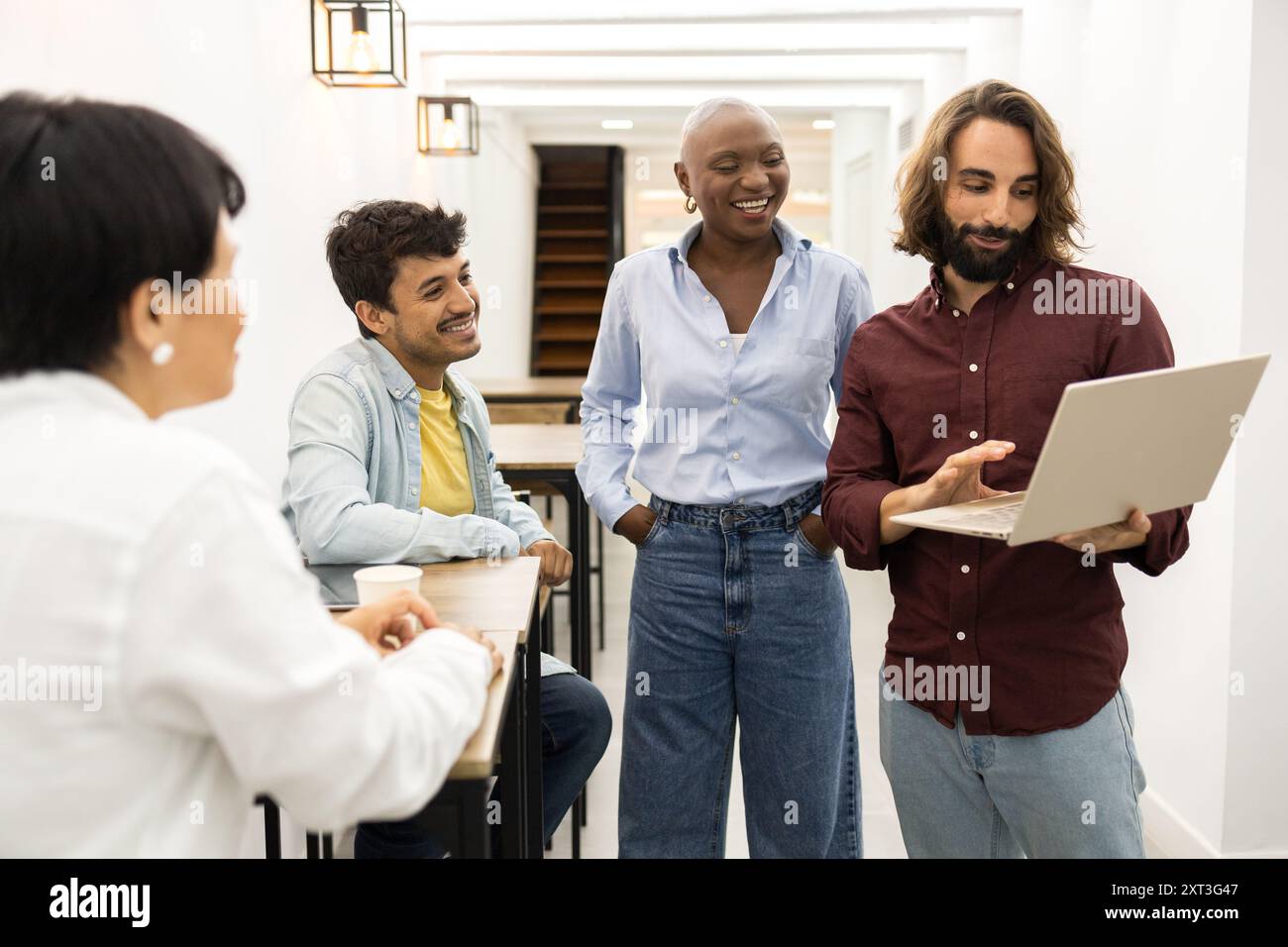 Un team diversificato di educatori ridono e collaborano in una classe illuminata, condividendo idee su un notebook, mostrando un ambiente di squadra sano in un Foto Stock