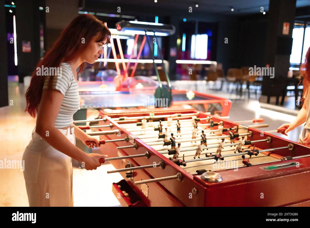 Vista laterale di una giovane donna, impegnata in una partita di calcio a palla, guarda il tavolo in un vivace ambiente da club con illuminazione al neon. Foto Stock