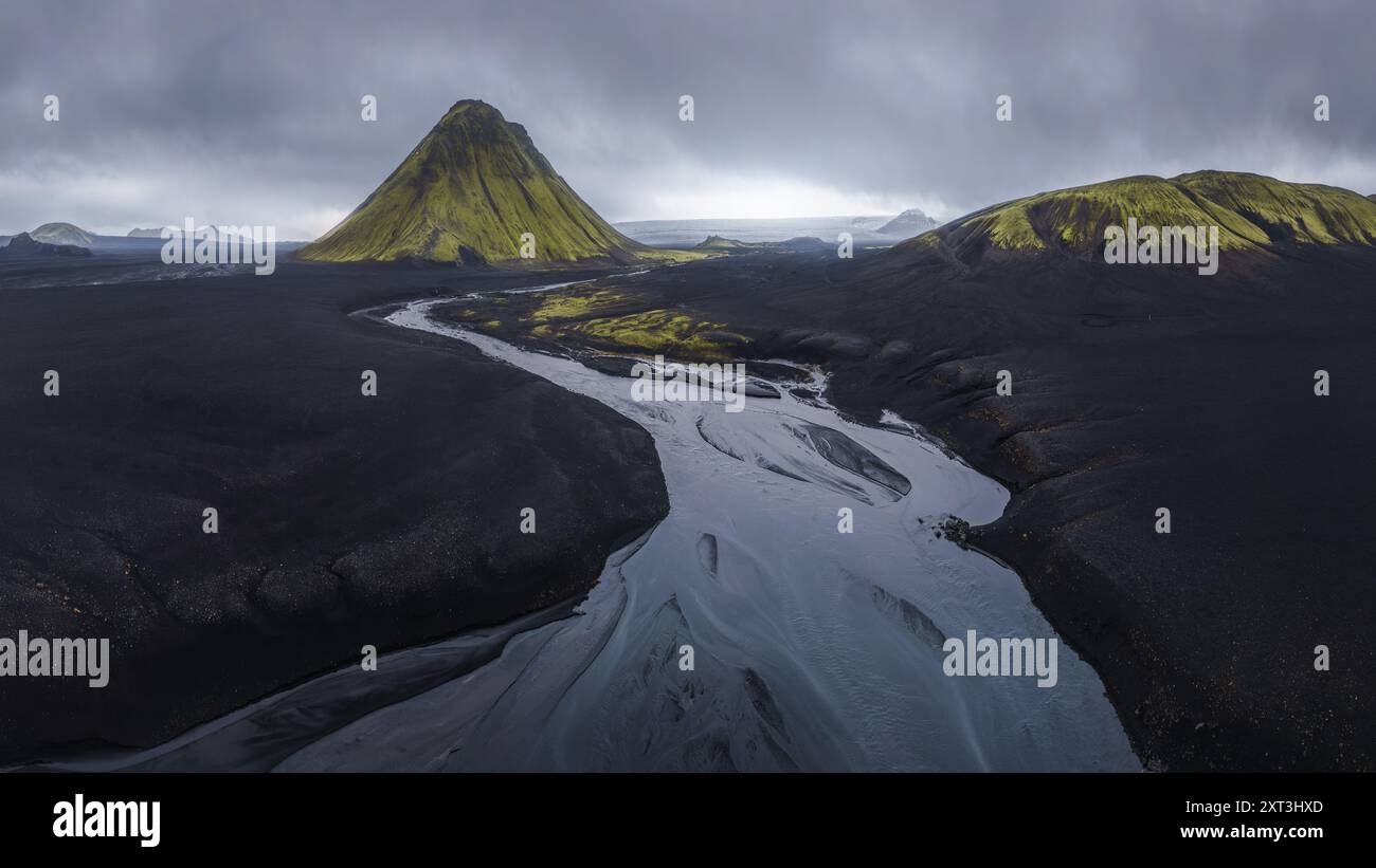 Ripresa aerea dell'impressionante vulcano Maelifell circondato da sabbie vulcaniche scure contrastate da un tortuoso fiume argenteo nelle remote Highlands di Icela Foto Stock
