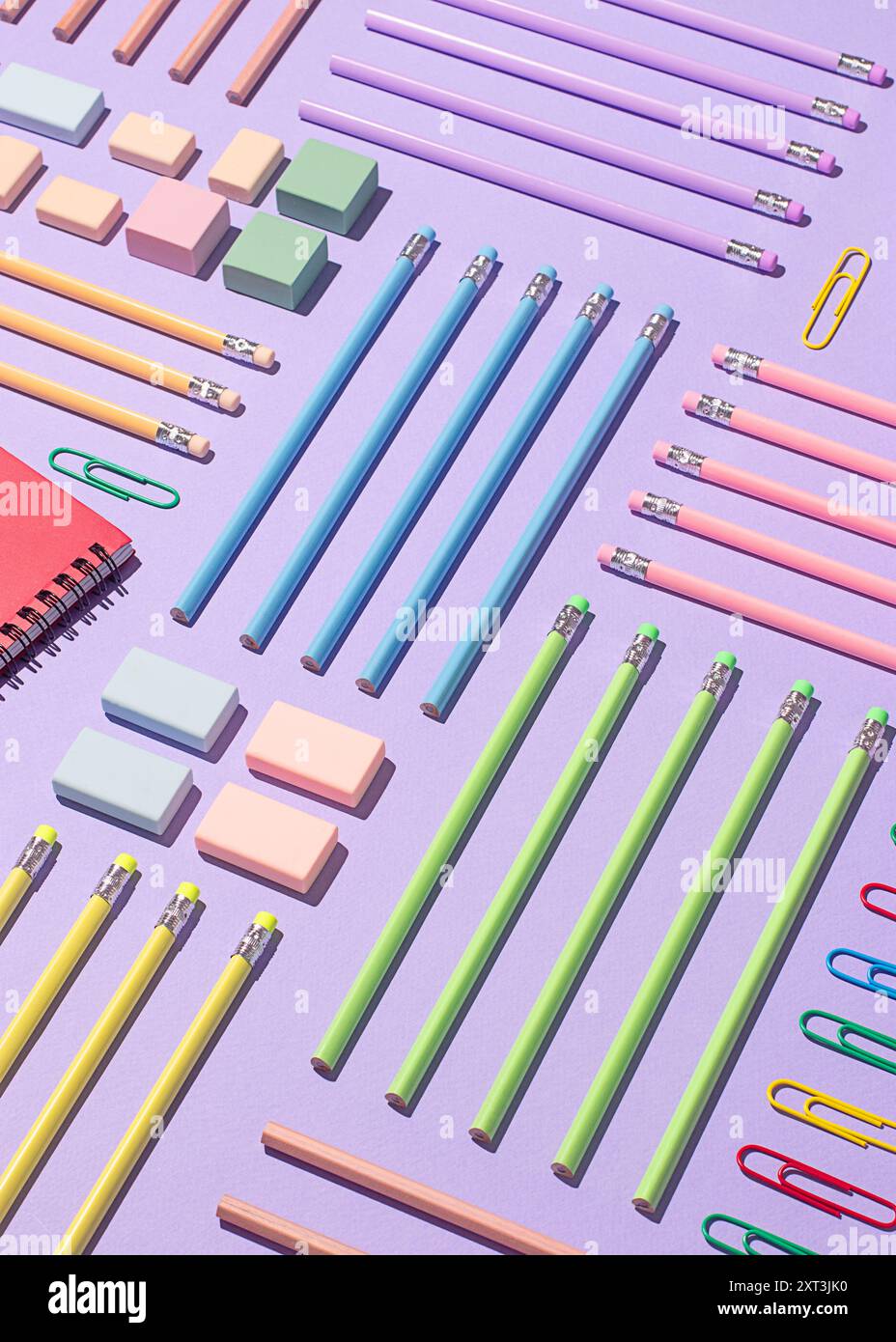 Una vista dall'alto ben organizzata delle forniture scolastiche, con matite, gomme, quaderni e graffette su una vivace superficie viola. Foto Stock