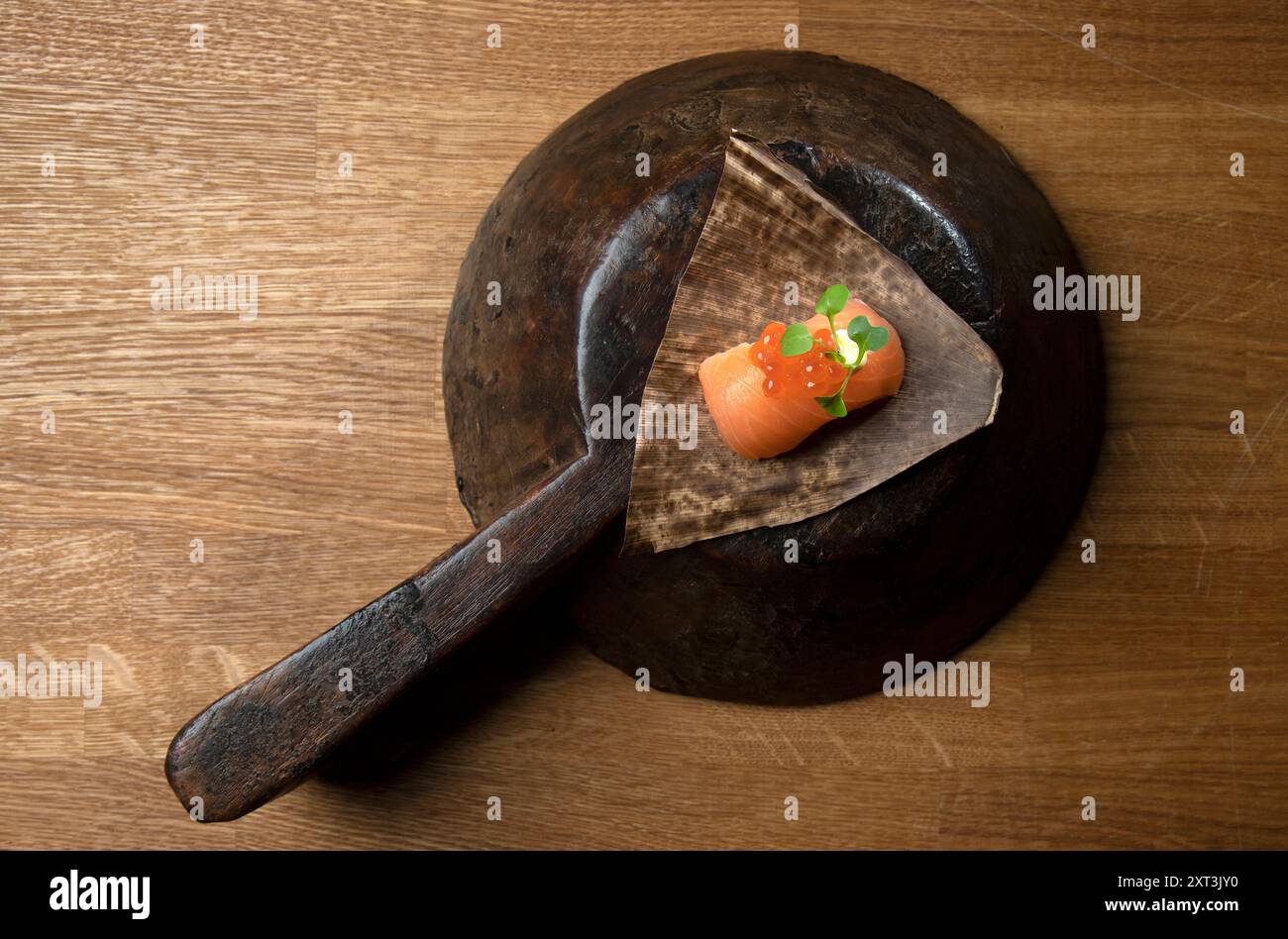 Un solo pezzo di sushi salmone tagliato con cura, presentato elegantemente in un contenitore rustico invecchiato piccole foglie verdi e uova rosse aggiungono freschezza e colore Foto Stock