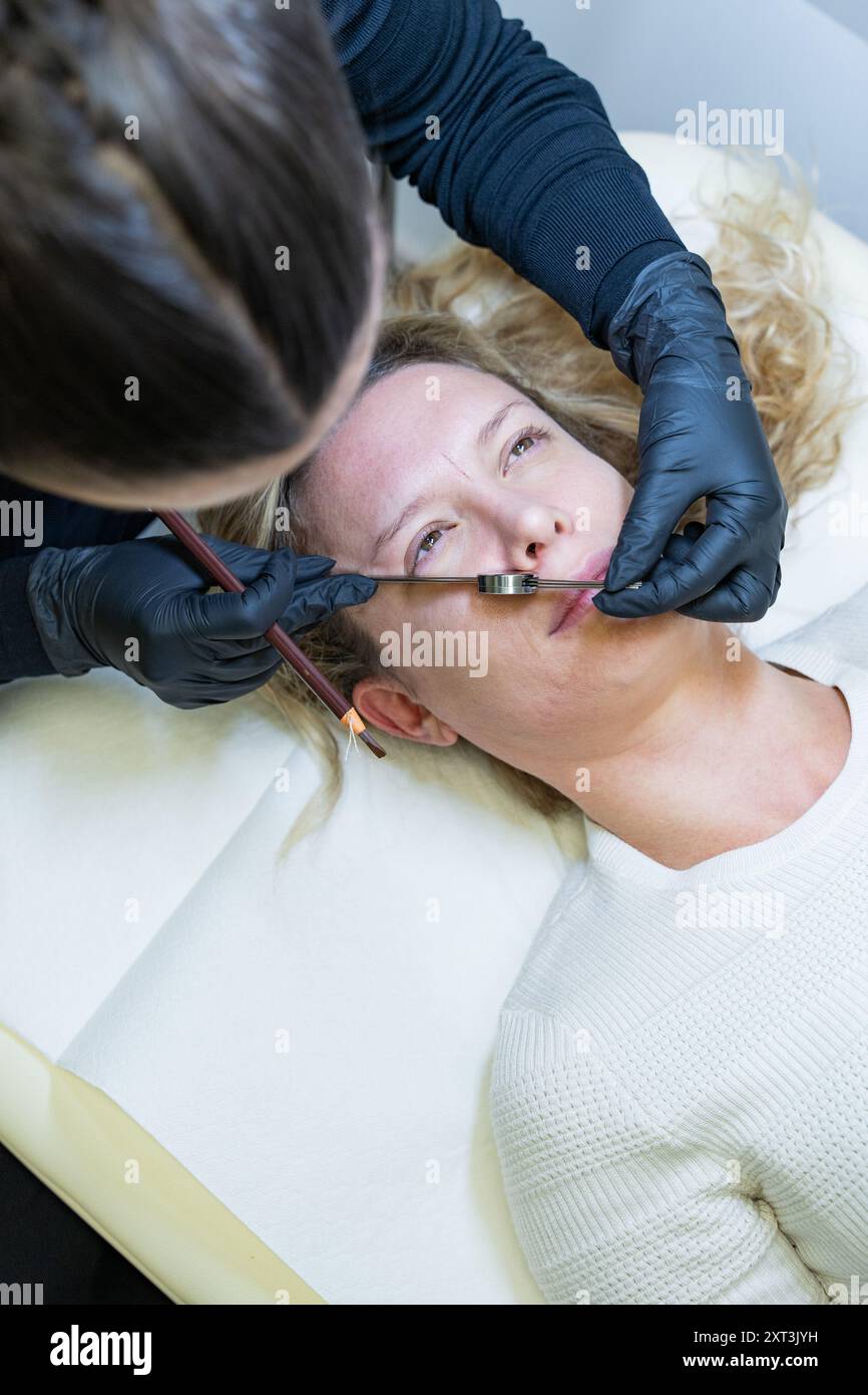 L'estetista adotta misure per garantire un trattamento equilibrato in armonia con la geometria del viso. Il cliente si sdraia indietro mentre si prende cura dei guanti Foto Stock