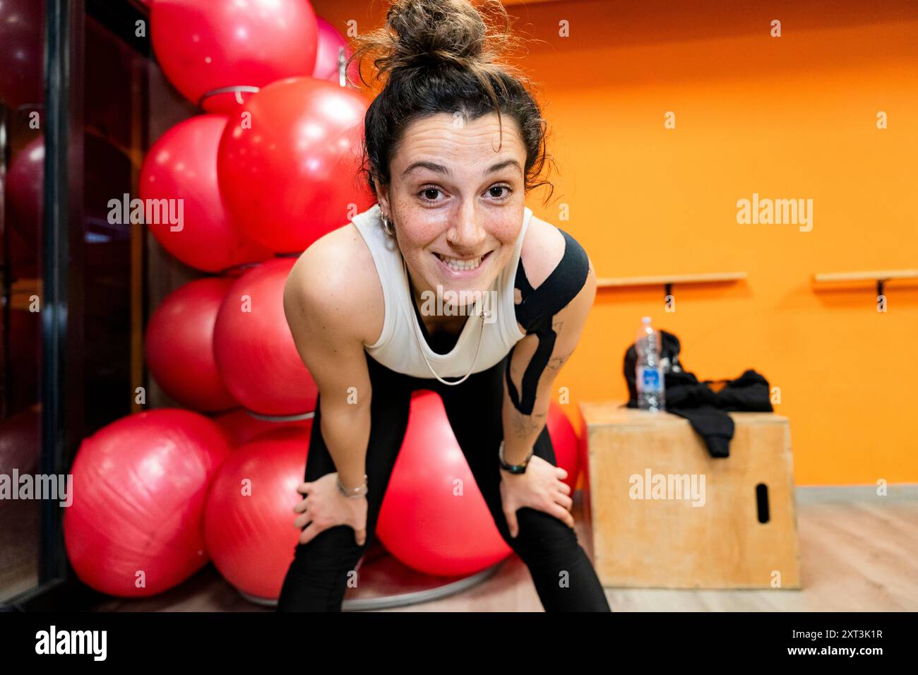 Questa immagine cattura una giovane donna sorridente durante un allenamento di potenziamento in palestra, circondata da attrezzature per l'esercizio fisico, trasuda energia e positività, Foto Stock