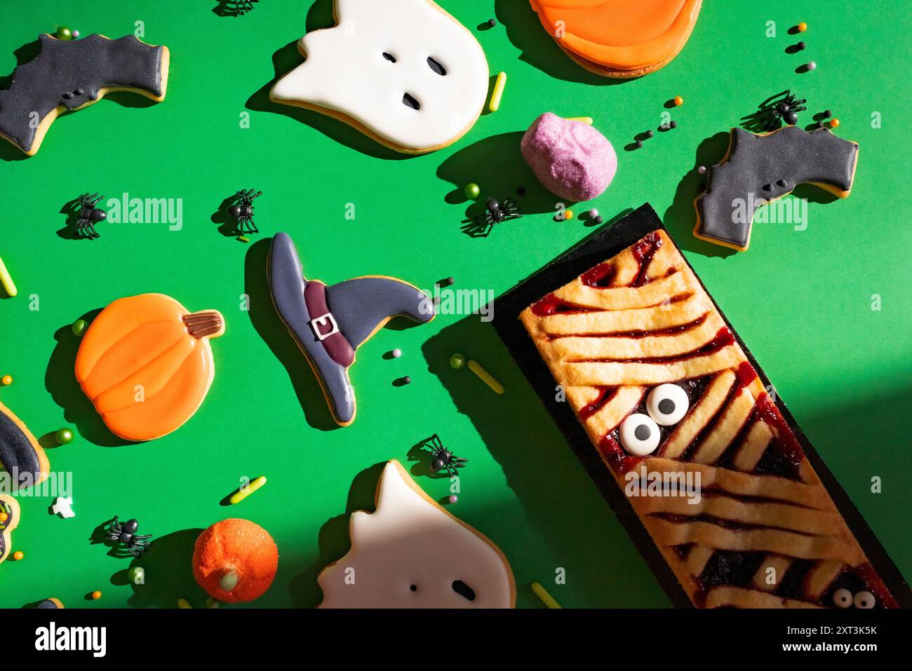 Un vivace set di biscotti di Halloween fatti in casa, con disegni come fantasmi, pipistrelli, zucche e cappelli da streghe, disposti su un vivace sfondo verde Foto Stock
