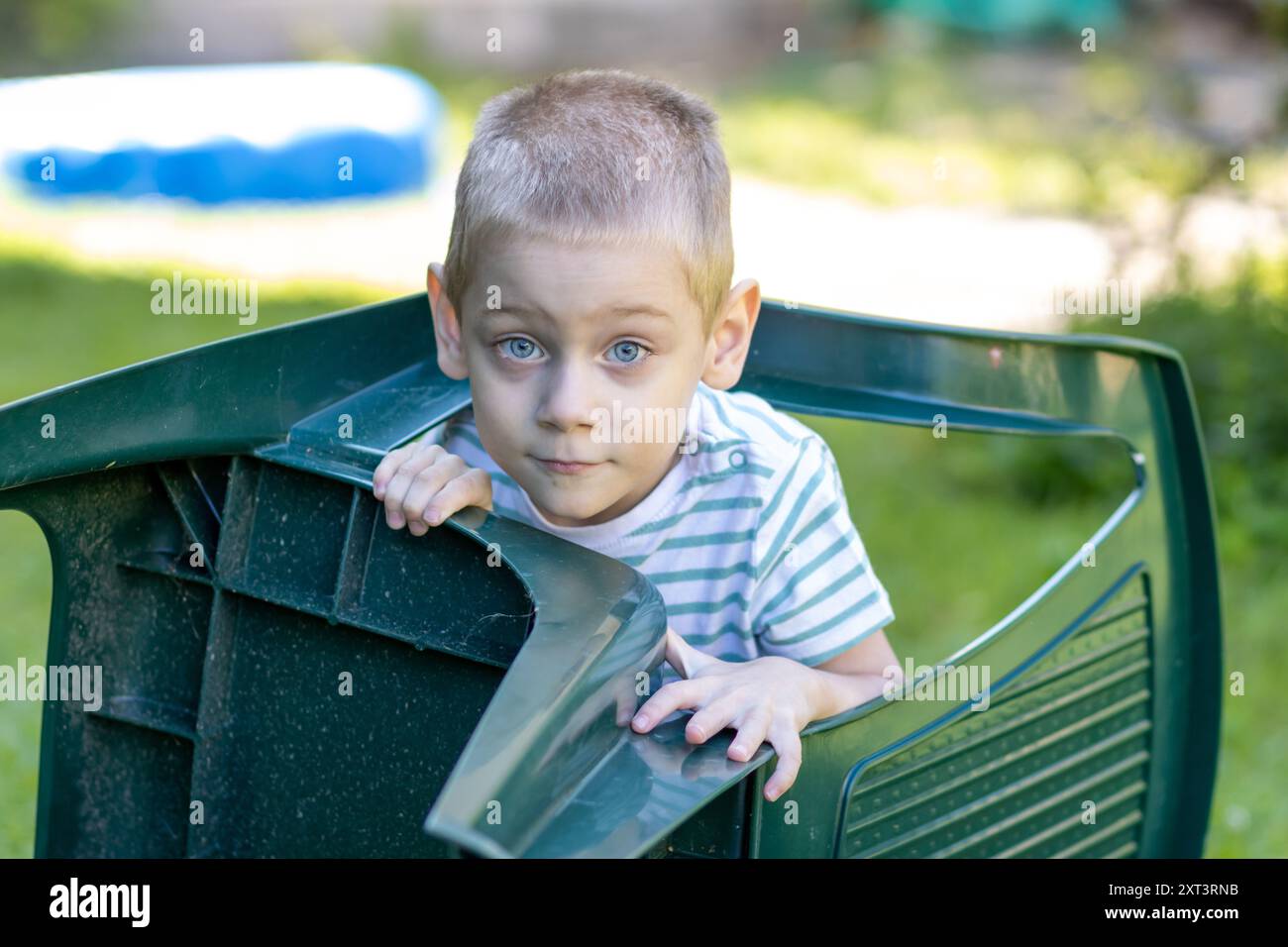 Un bambino sbircia da dietro una sedia di plastica in giardino Foto Stock