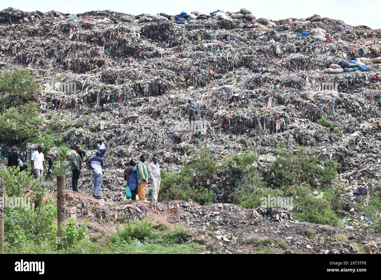 Kampala, Uganda. 13 agosto 2024. La gente del posto si trova accanto alla massa di rifiuti crollati nella discarica di Kiteezi a Kampala, in Uganda, il 13 agosto 2024. La polizia ugandese ha detto martedì che ci sono ancora più persone intrappolate sotto la massa dei rifiuti, dopo la frana della discarica di Kiteezi a Kampala, la capitale dell'Uganda, sabato mattina. Patrick Onyango, portavoce della polizia metropolitana di Kampala, ha detto telefonicamente a Xinhua che la polizia non è ancora sicura di quante persone siano ancora intrappolate con altri rapporti sui parenti scomparsi depositati alla polizia. Crediti: Hajarah Nalwadda/Xinhua/Alamy Live News Foto Stock