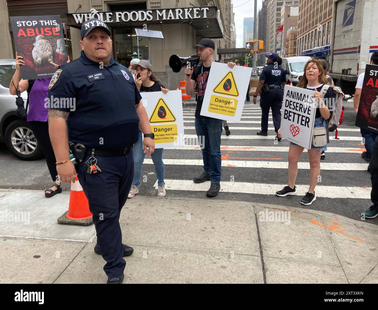 Membri del NYPD corral manifestanti per i diritti degli animali fuori dal negozio Crumbl a Chelsea a New York venerdì 9 agosto 2024 durante un'attivazione del marchio. I manifestanti si sono opposti alla catena dei biscotti che utilizza uova di galline tenute in presunte condizioni non sanitarie e abusive. (© Frances M. Roberts) Foto Stock