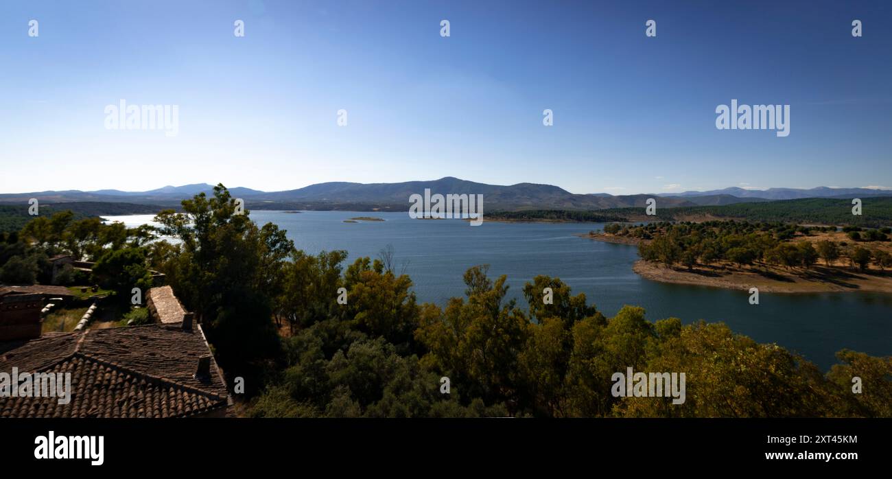 Il lago artificiale Gabriel y Galan di Caceres cattura un tranquillo paesaggio di acque blu, incorniciato da montagne lontane e alberi lussureggianti, offrendo un ambiente sereno Foto Stock