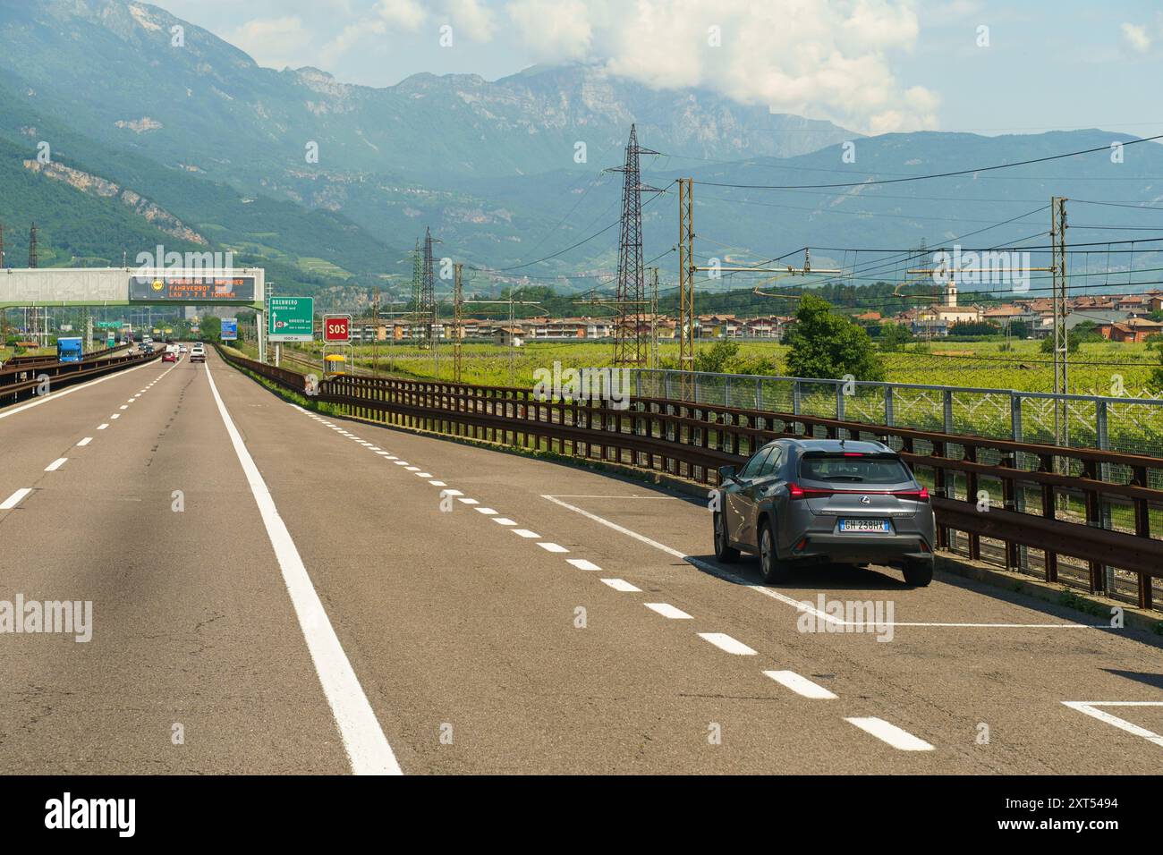 Lizzana, Italia - 8 giugno 2023: Un'auto parcheggiata sul lato dell'autostrada, con un cartello SOS, circondata da prati rigogliosi e montagne torreggianti Foto Stock