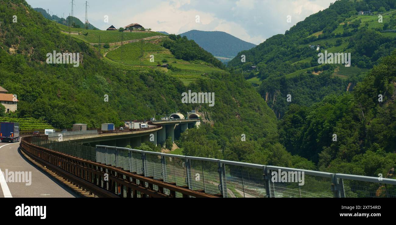 Un semi-camion percorre una strada tortuosa su una montagna, che conduce verso l'ingresso di un tunnel, con una vista su lussureggianti vallate verdi su entrambi i lati. Foto Stock