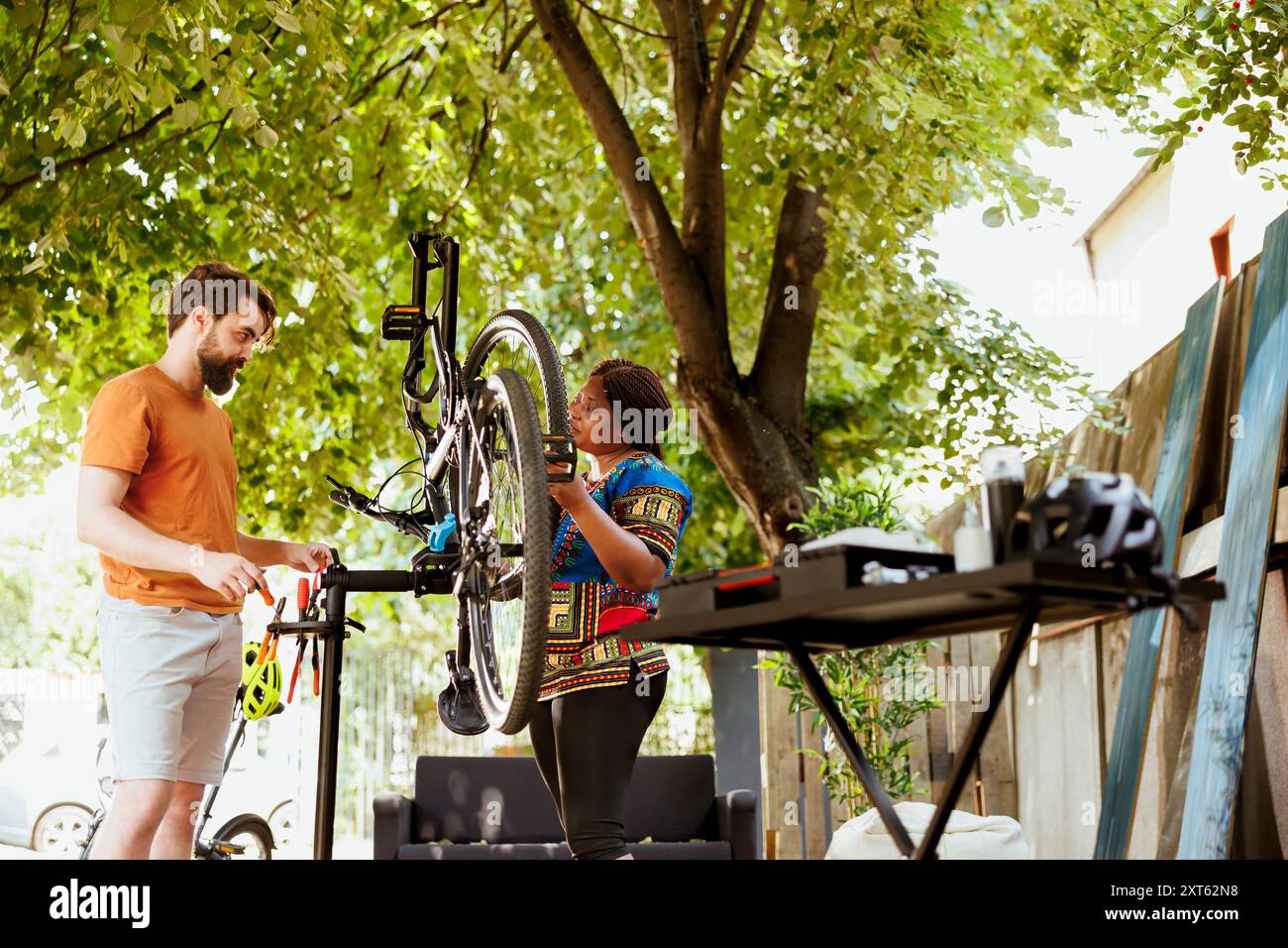 Attività di manutenzione all'aperto con coppie multietniche amanti dello sport che puliscono e riparano parti di biciclette. Attiva coppia interrazziale dedicata che esegue la manutenzione annuale estiva delle biciclette. Foto Stock