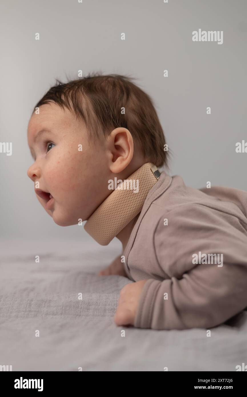 Ritratto di un neonato sdraiato sullo stomaco in un collare ortopedico. Foto verticale. Foto Stock