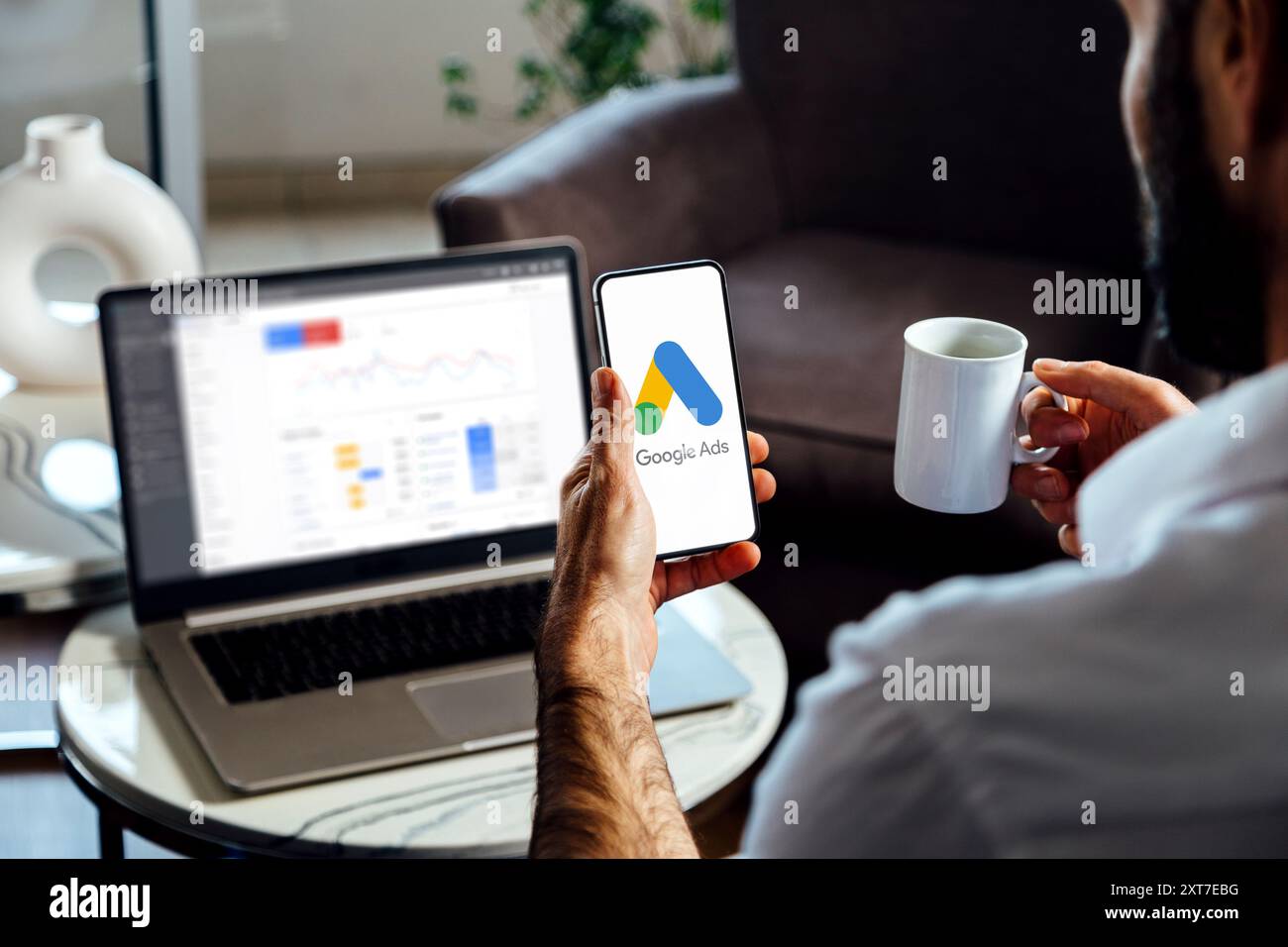 Uomo che utilizza un telefono cellulare con Google Ads sullo schermo e in background un computer che mostra le statistiche degli annunci. Rosario, Argentina - 23 luglio 2024. Foto Stock