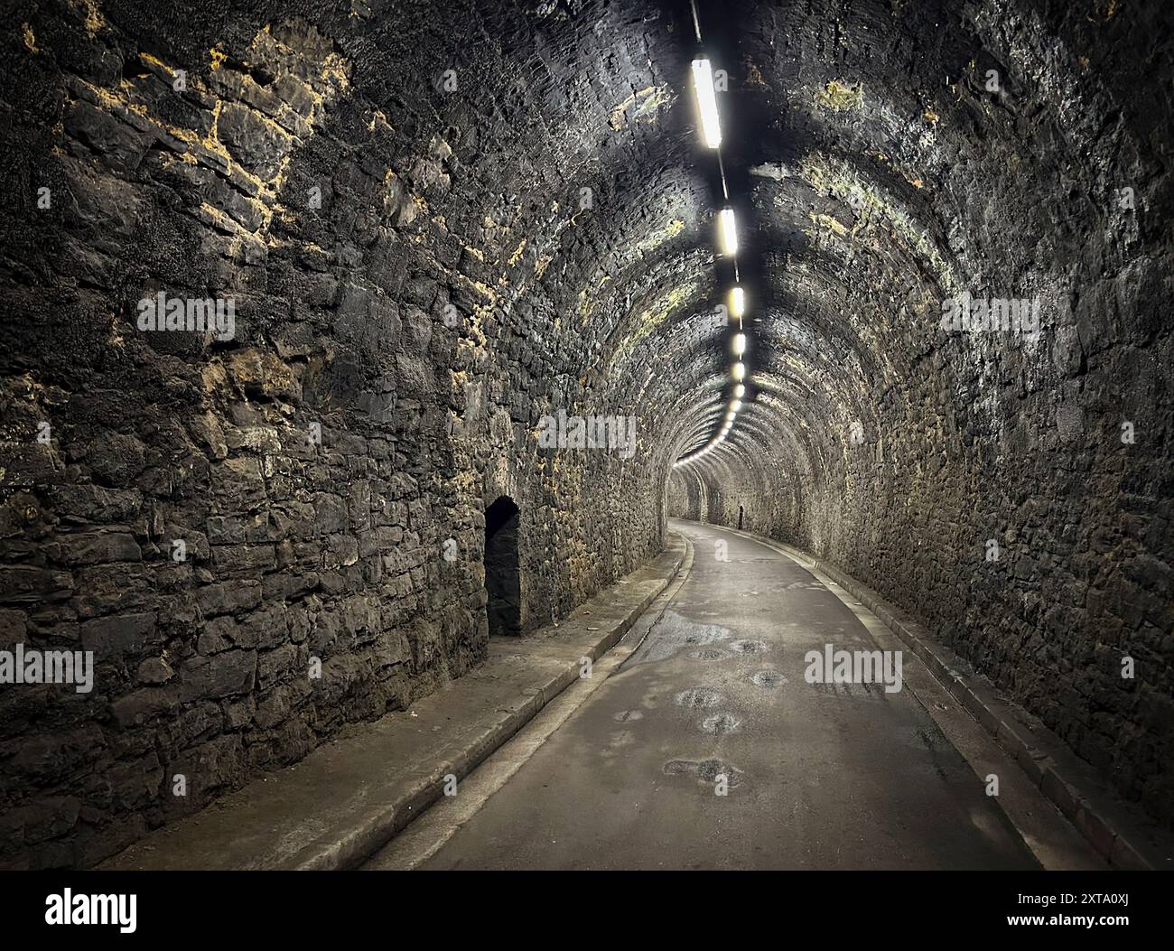Vista prospettica di un tunnel di pietra illuminato con luci fluorescenti. Foto Stock