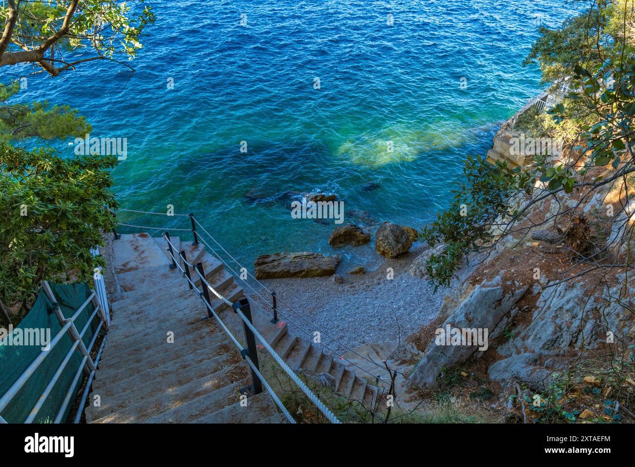 Discesa ripida giù per le scale verso una spiaggia rocciosa, la costa del mare Adriatico in Croazia, ringhiera di sicurezza fatta di spessa fune da pesca Foto Stock