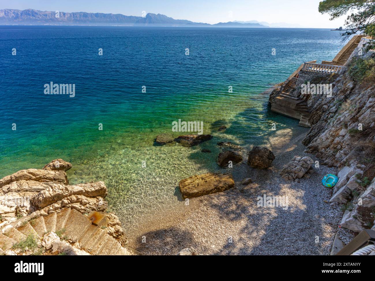 Discesa ripida giù per le scale verso una spiaggia rocciosa, la costa del mare Adriatico in Croazia, ringhiera di sicurezza fatta di spessa fune da pesca Foto Stock