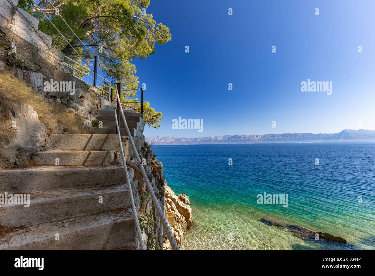 Discesa ripida giù per le scale verso una spiaggia rocciosa, la costa del mare Adriatico in Croazia, ringhiera di sicurezza fatta di spessa fune da pesca Foto Stock