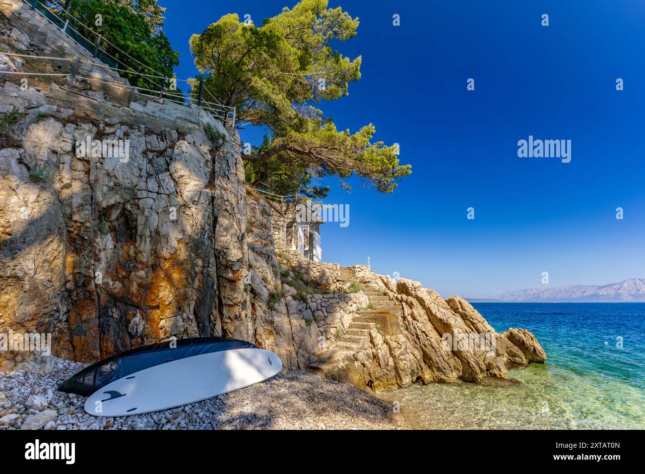 Discesa ripida giù per le scale verso una spiaggia rocciosa, la costa del mare Adriatico in Croazia, ringhiera di sicurezza fatta di spessa fune da pesca Foto Stock