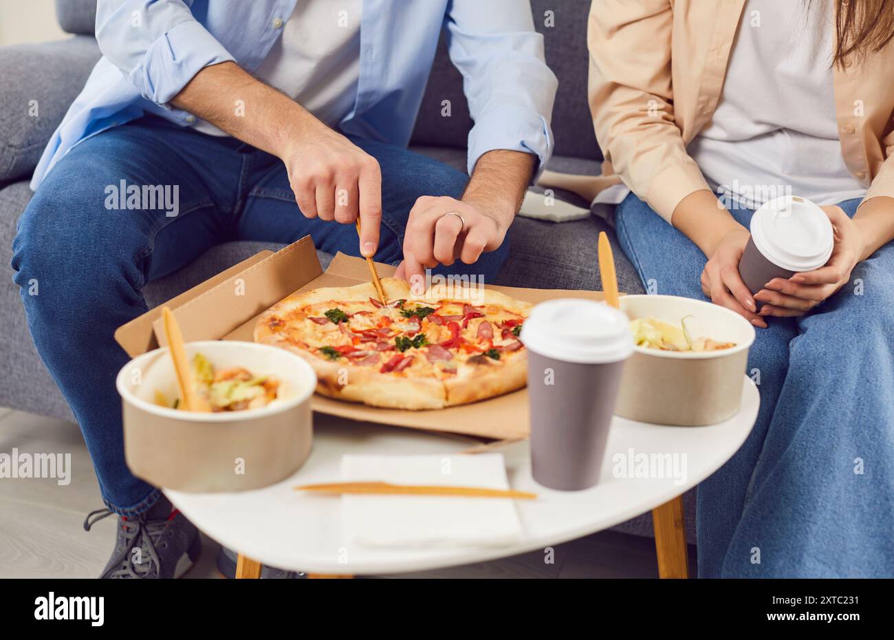Una giovane coppia gusta il pranzo a casa con pizza, insalata e caffè caldo. Foto Stock