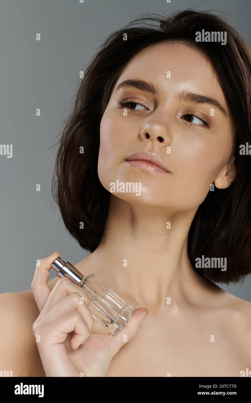 Una donna dai capelli scuri e corti spritzza il profumo davanti a uno sfondo vibrante. Foto Stock