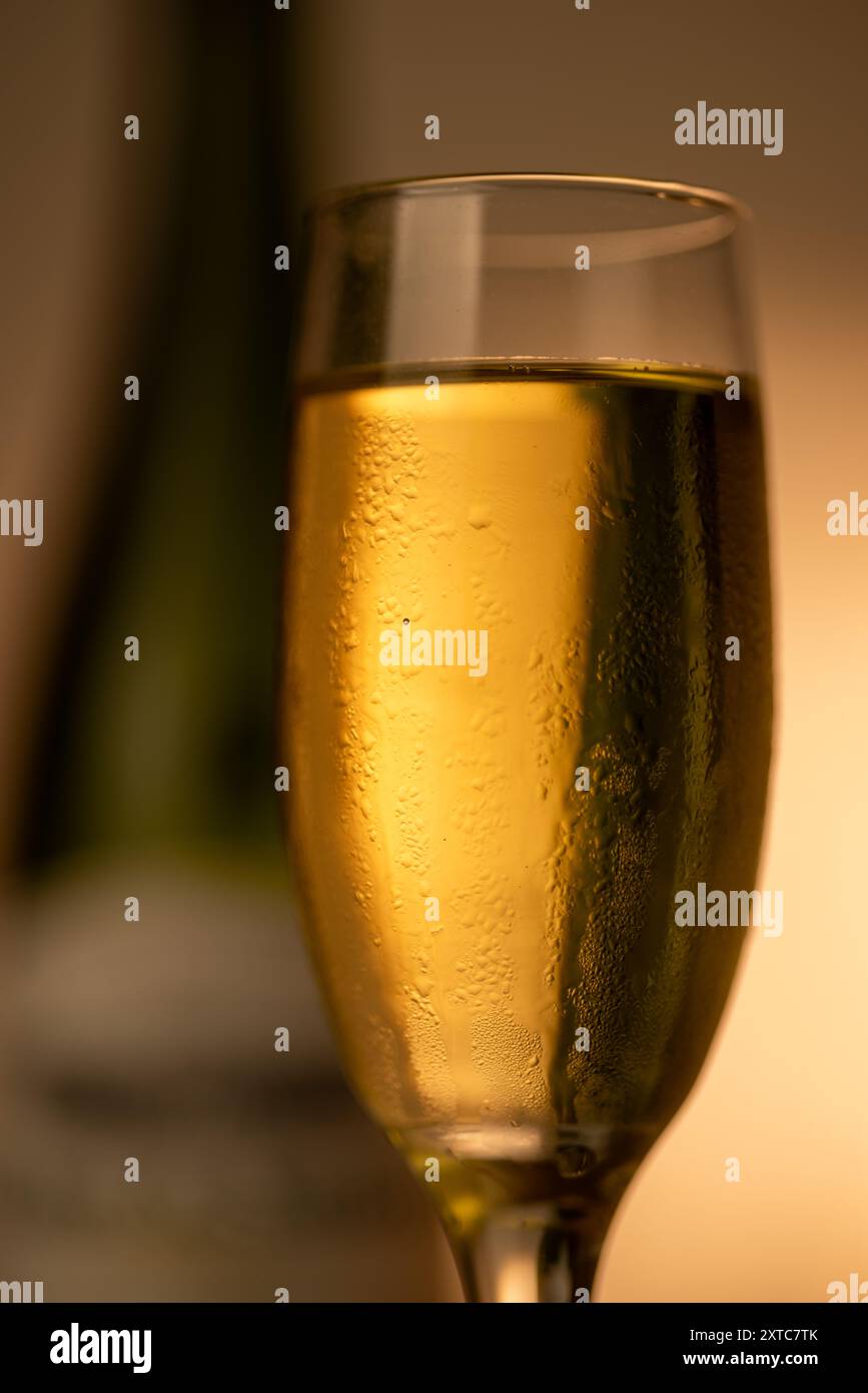 Un'immagine verticale che mostra un flute dettagliato di champagne con champagne freddo, con una bottiglia di champagne verde fuori fuoco sulla destra. Il gradiente d'oro Foto Stock