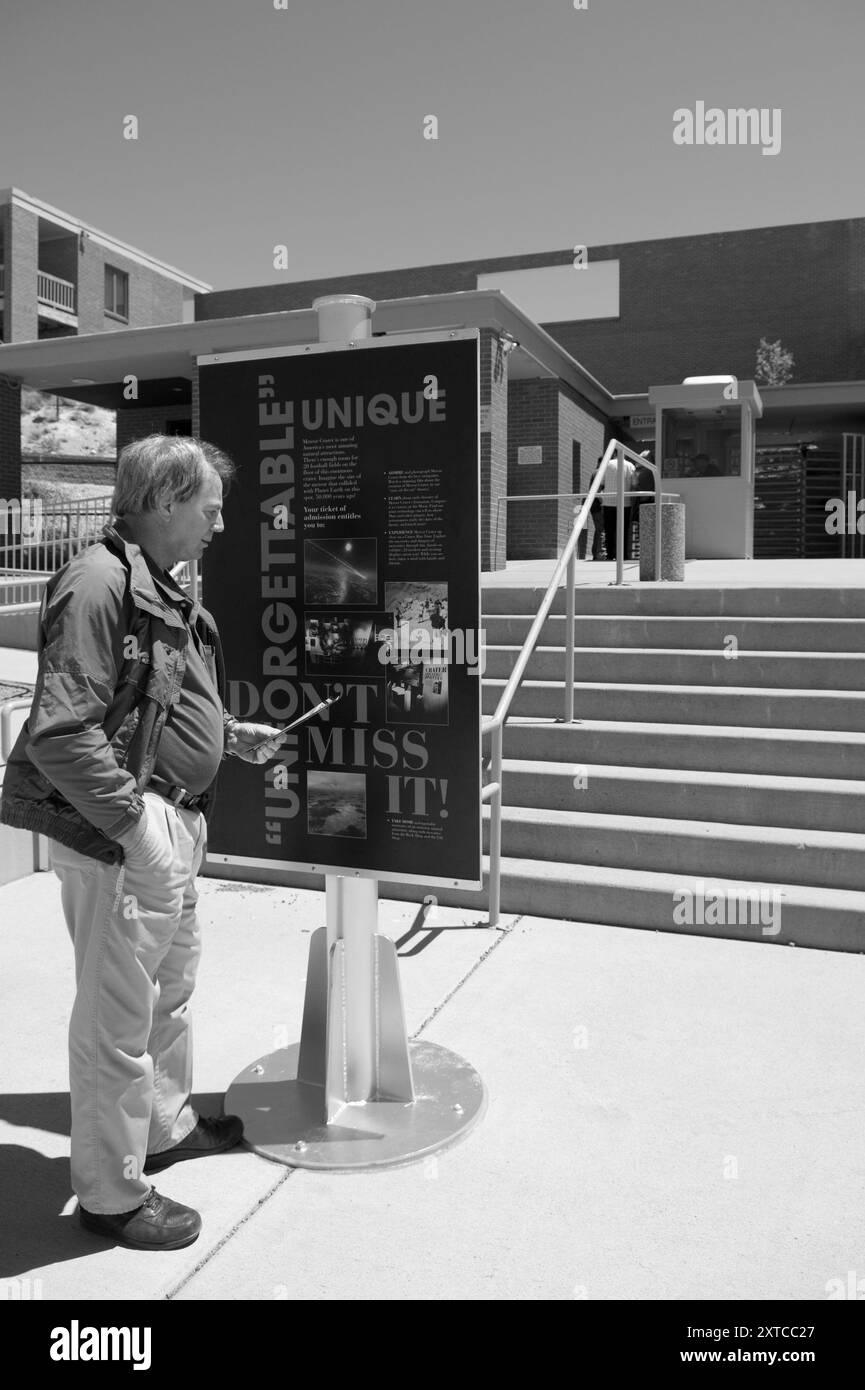 Uomo caucasico di 50 - 60 anni che legge il cartello d'ingresso al cratere Meteor, situato sulla Route 66 all'uscita dell'Interstate 40 vicino a Winslow, Arizona, Stati Uniti. Foto Stock