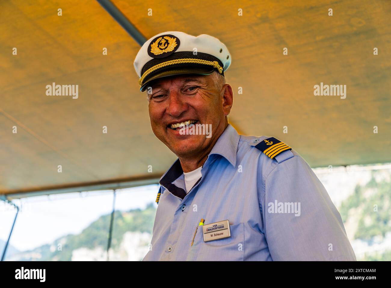 Il capitano capo M. Scheurer della Società di Navigazione del Lago dei Quattro Cantoni ride sotto un baldacchino giallo a bordo. Il suo berretto bianco porta un emblema di ancora dorato, e le sue spalline mostrano quattro strisce dorate. Axenstrasse, Morschach, Schwyz, Svizzera. Foto Stock