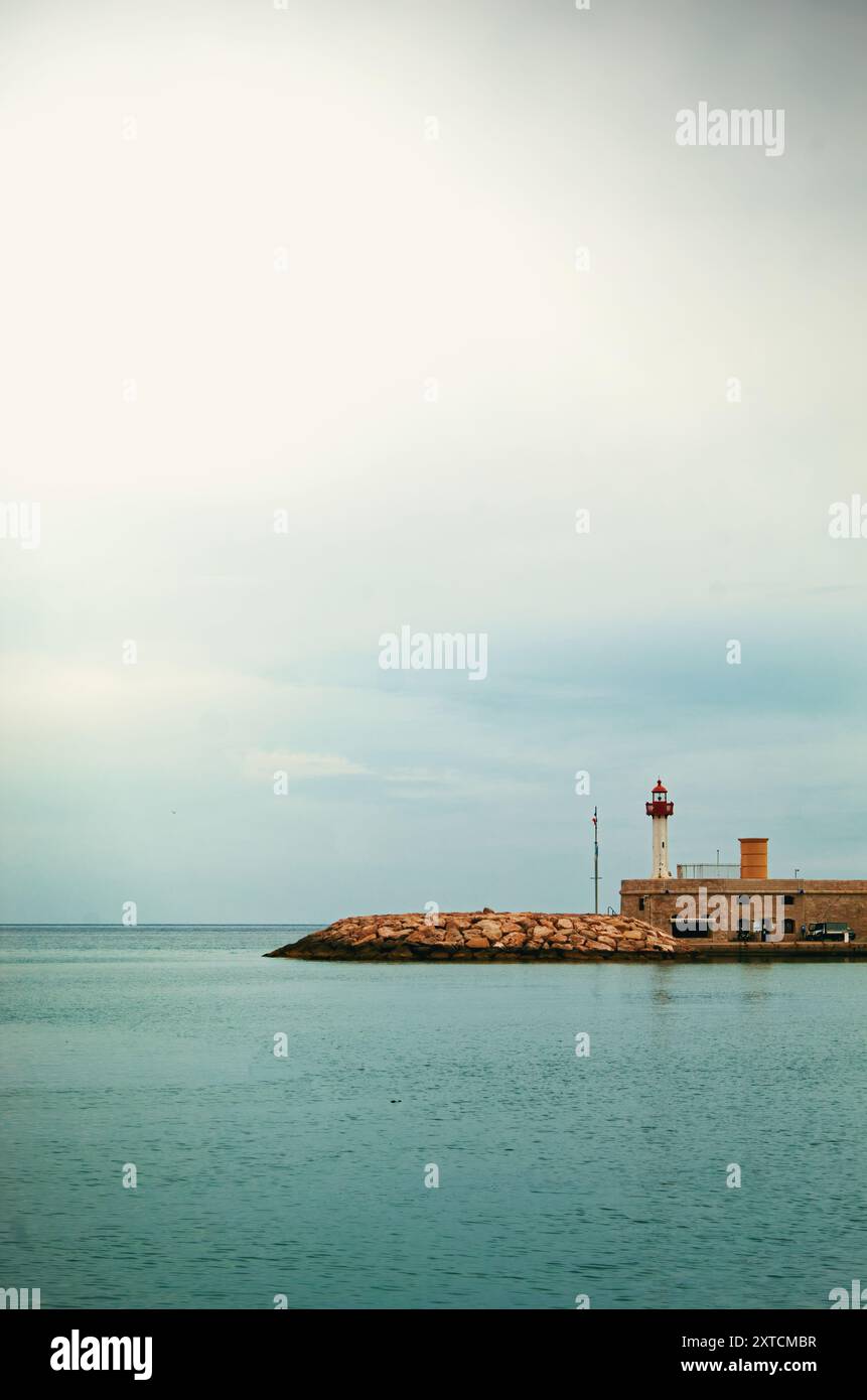 Faro solitario sul tranquillo molo tra vaste acque aperte sotto il cielo coperto, Mentone, Francia Foto Stock