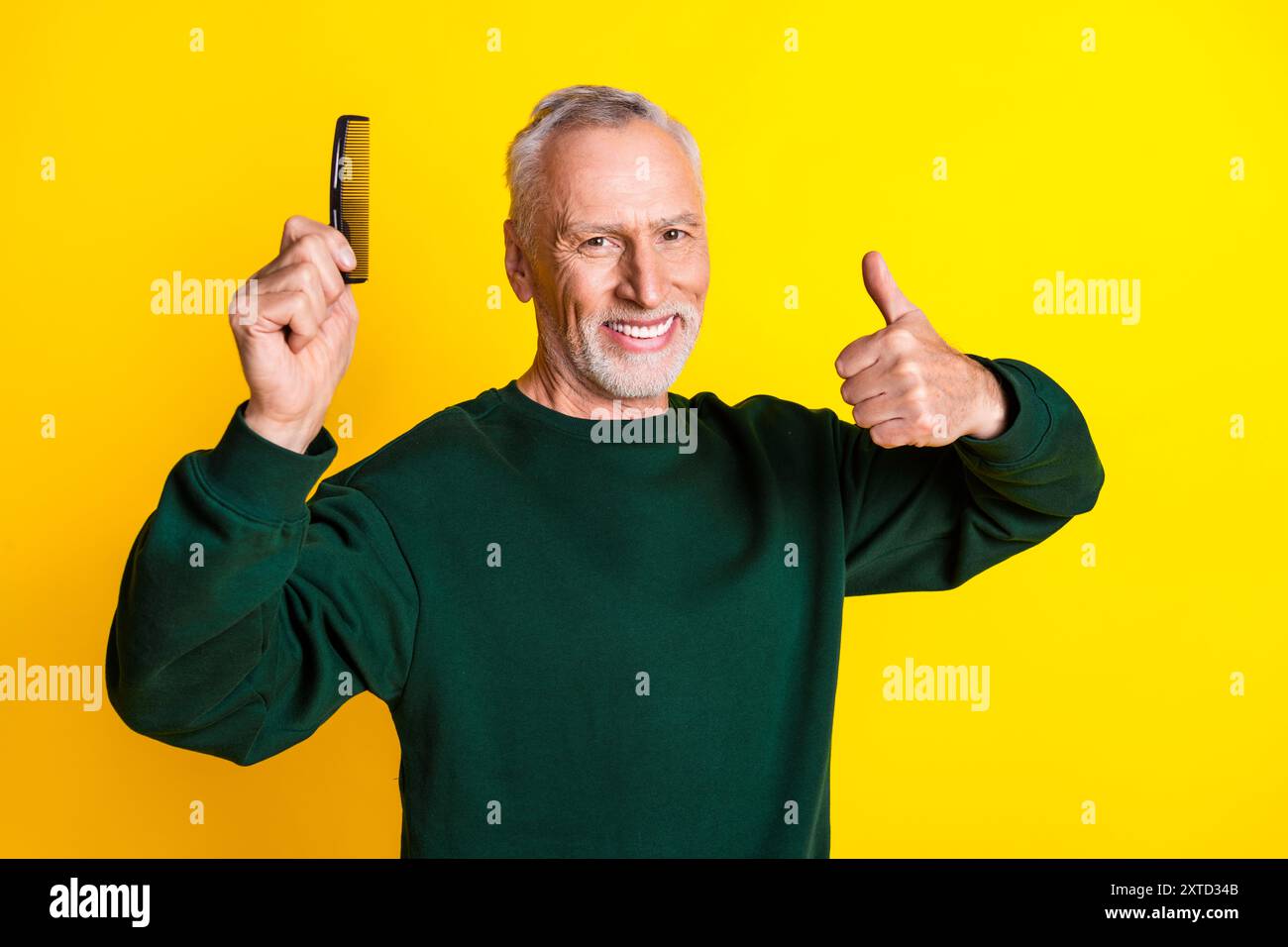 Foto ritratto di un grazioso pensionato che tiene in mano la spazzola per capelli con il pollice vestita elegante indumento verde isolato su sfondo giallo Foto Stock